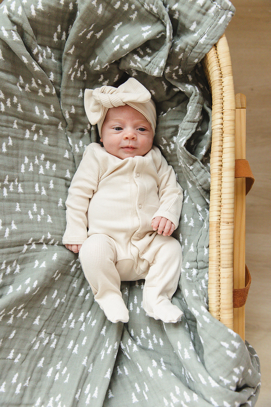 Vanilla organic cotton baby bodysuit with a bow hat on an infant, resting in a cozy basket with patterned blanket.