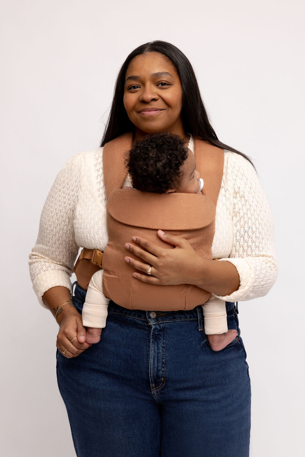 Mom wearing the Willow Aerial Carrier in caramel brown, comfortably holding her baby.