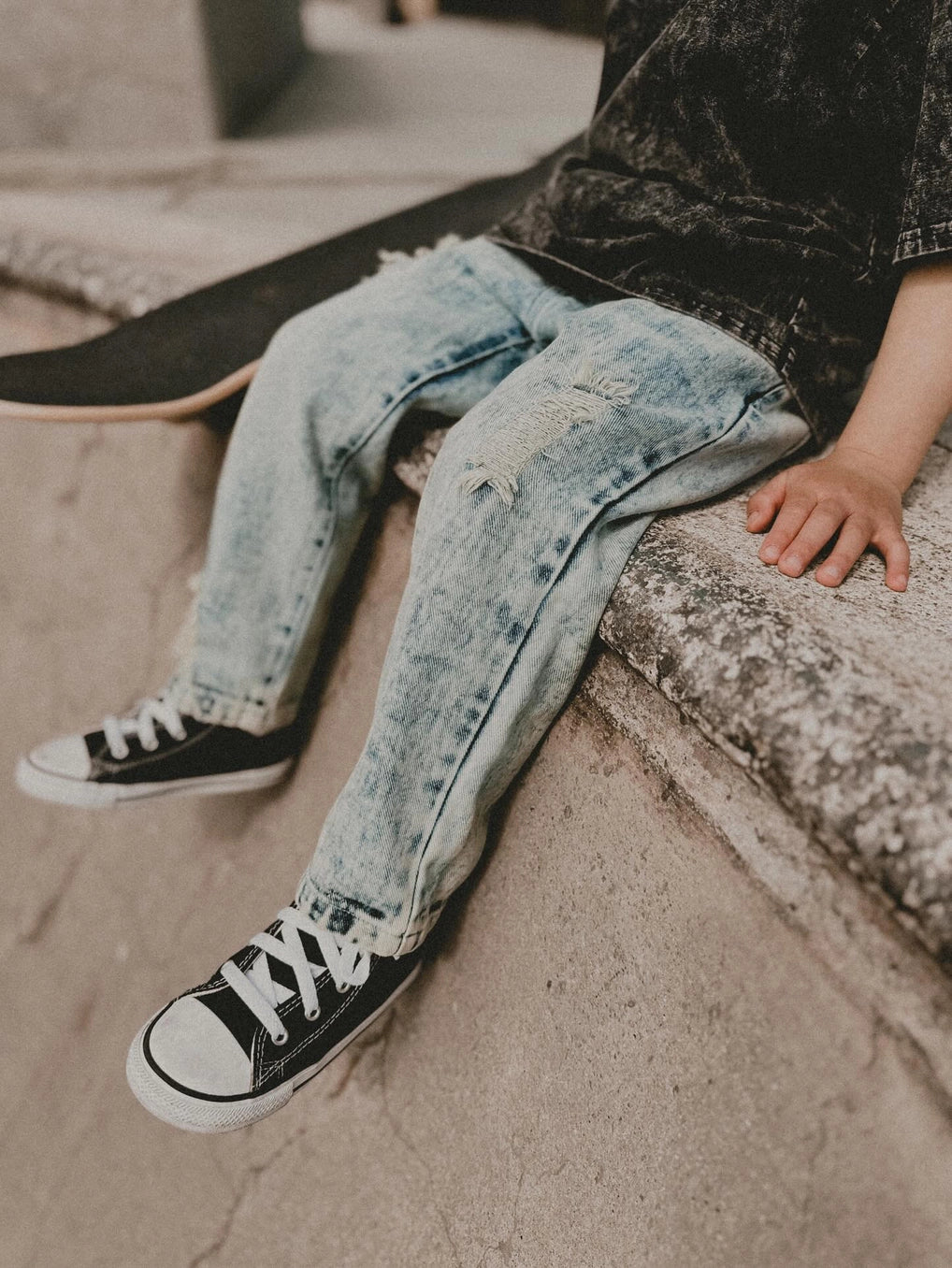 Toddler relaxed straight light acid wash denim jeans displayed on child sitting on the edge, wearing black sneakers.