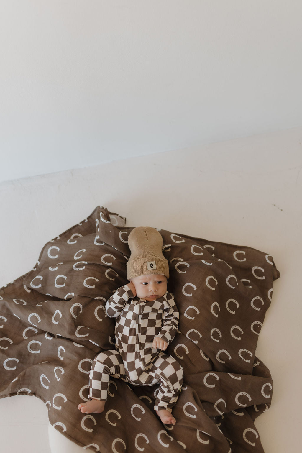 Baby in brown and white checkerboard bamboo zip pajamas by Dutton, resting on a coordinating blanket.