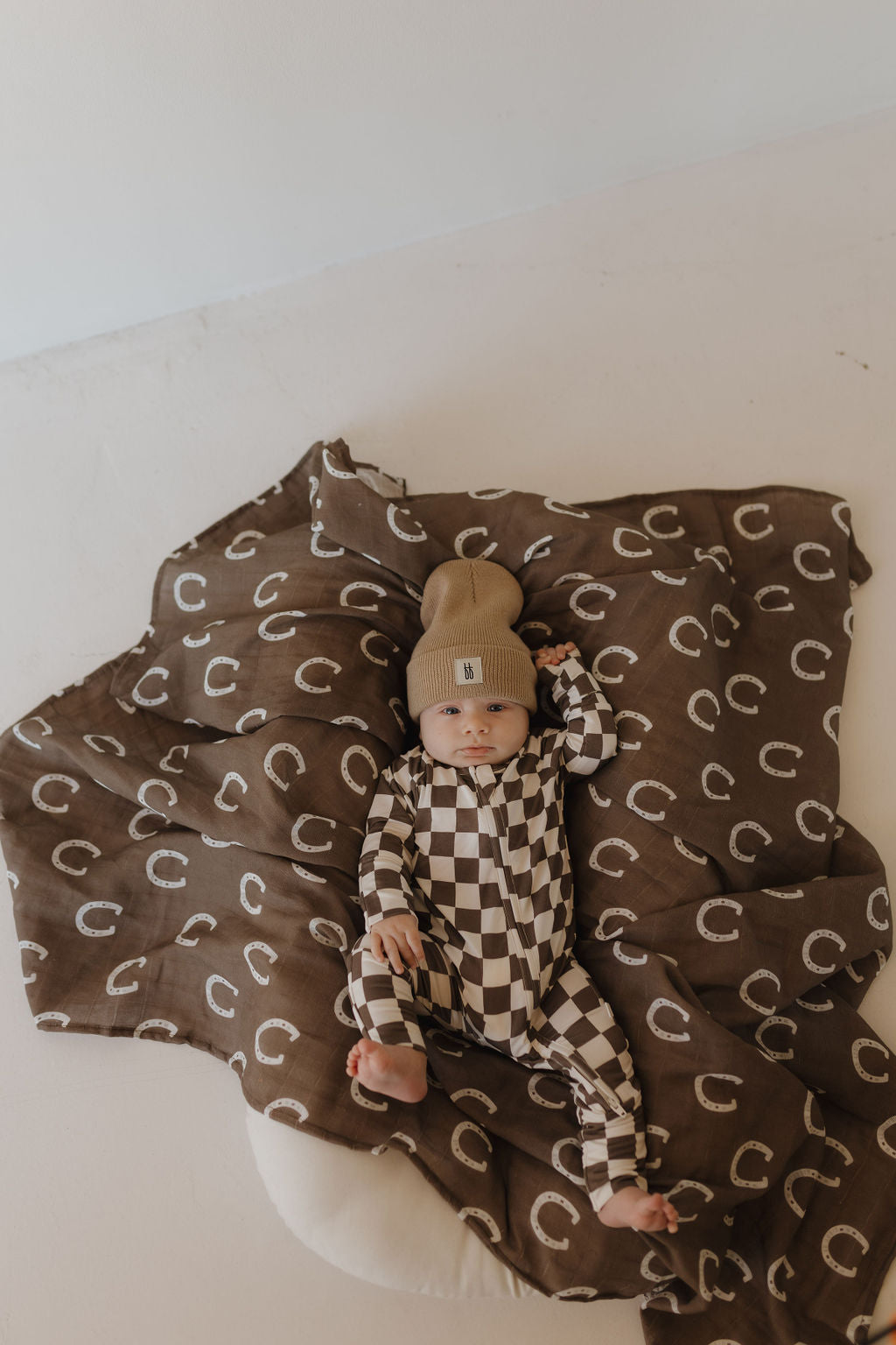 Baby in brown and white checkerboard bamboo zip pajamas by Dutton, lying on a patterned blanket.