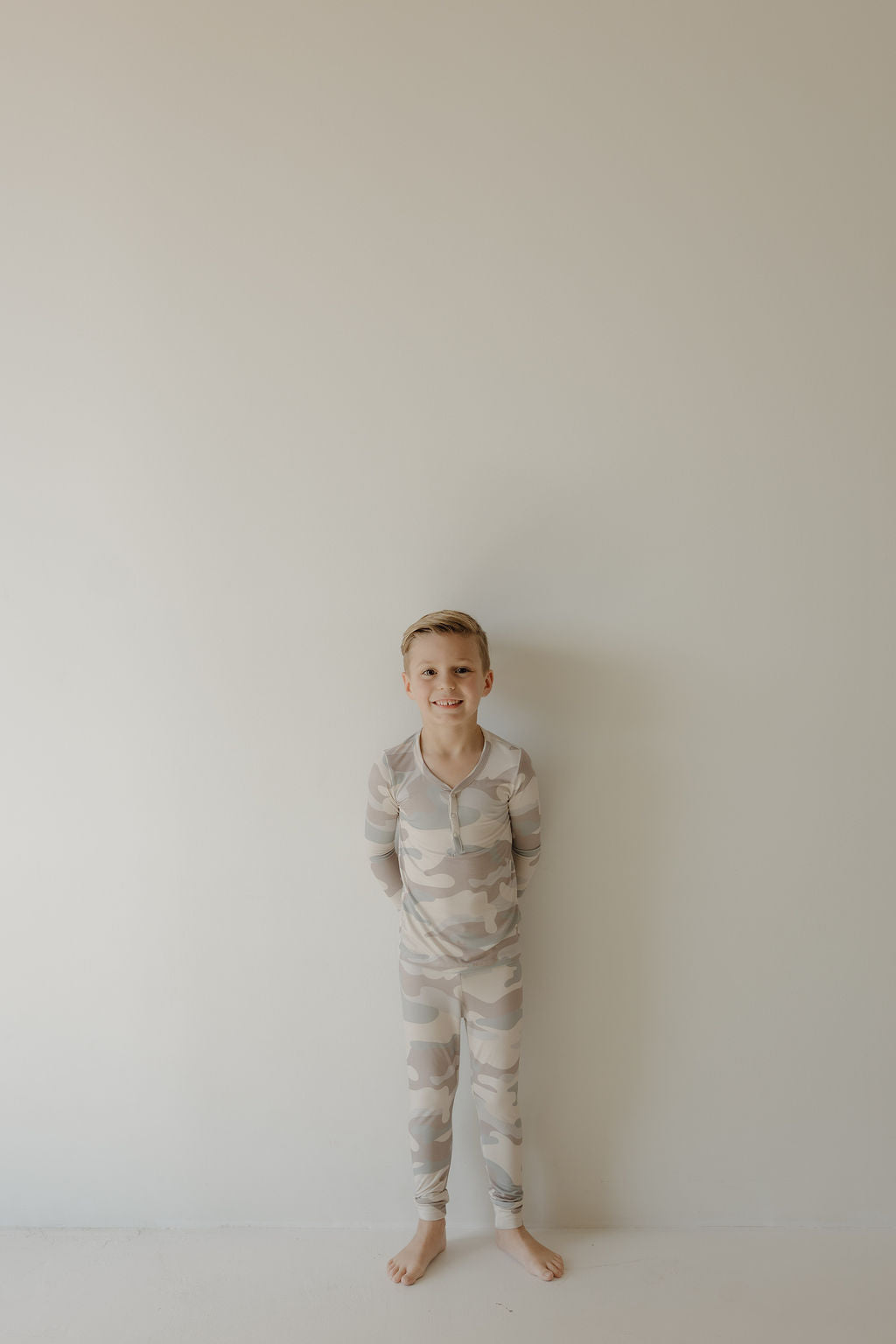 Smiling child in bamboo two-piece pajamas camo set against a blank wall, showcasing comfort and style.