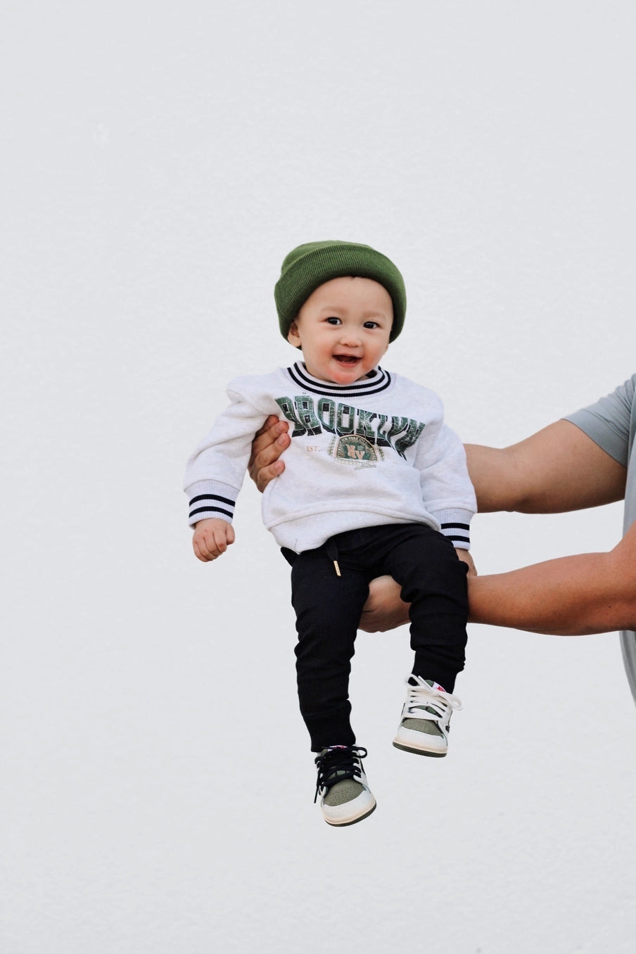 Toddler wearing vintage inspired Brooklyn crew sweatshirt and green beanie, held by an adult.