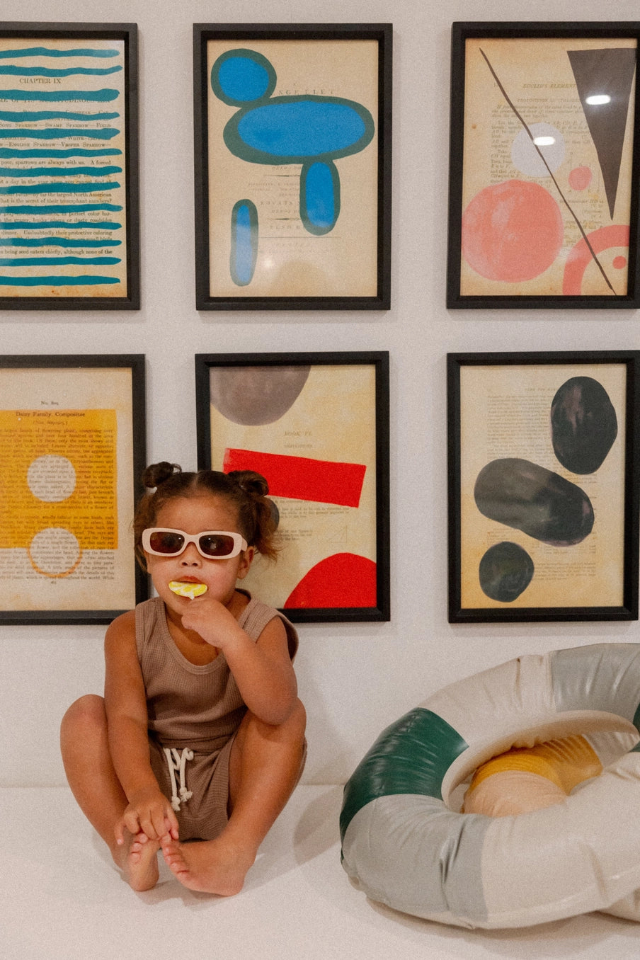 Child wearing sunglasses in the Madden Tank Set, sitting near colorful art and a pool float.