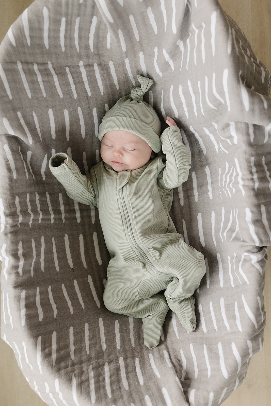 Newborn in sage organic cotton ribbed zipper pajamas, cozy and stylish on a patterned blanket.
