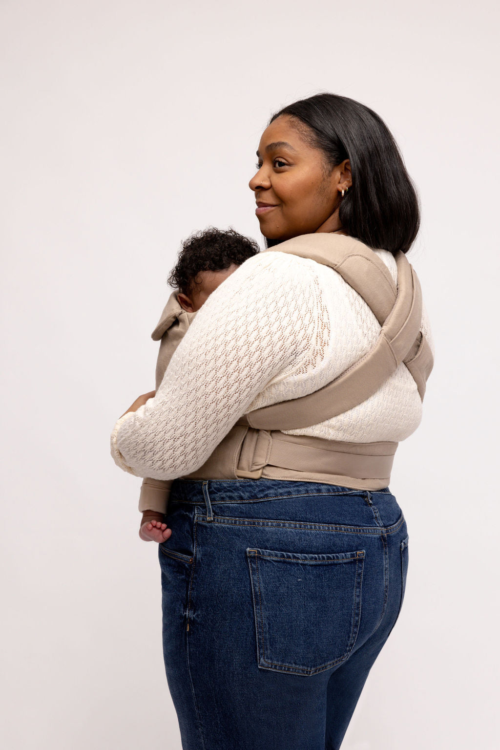Mom carrying baby in Desert Lark aerial carrier, stylish taupe grey fabric, offering comfort and convenience.