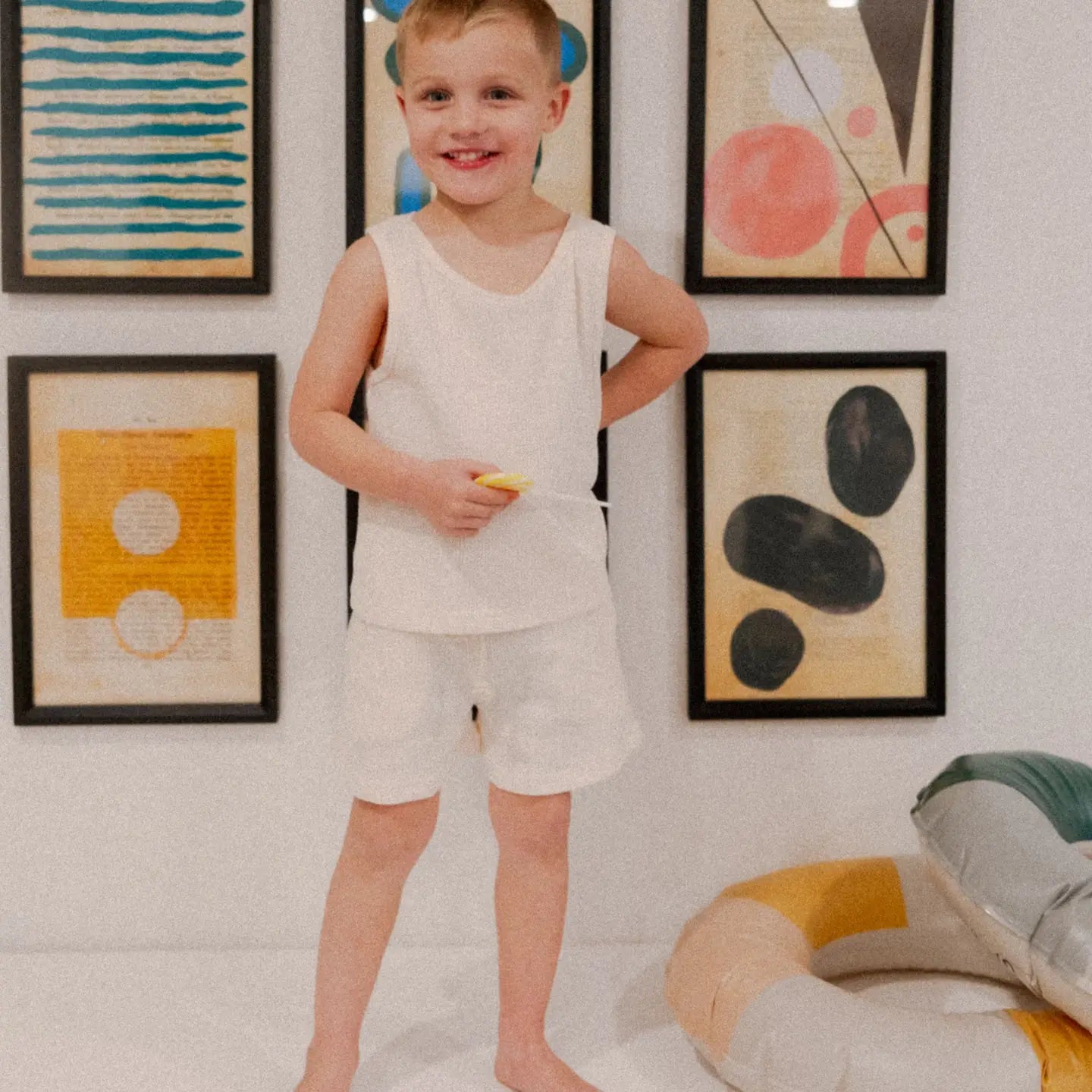 Boy wearing the Madden Tank Set, a cream waffle-knit tank and shorts, against colorful wall art.