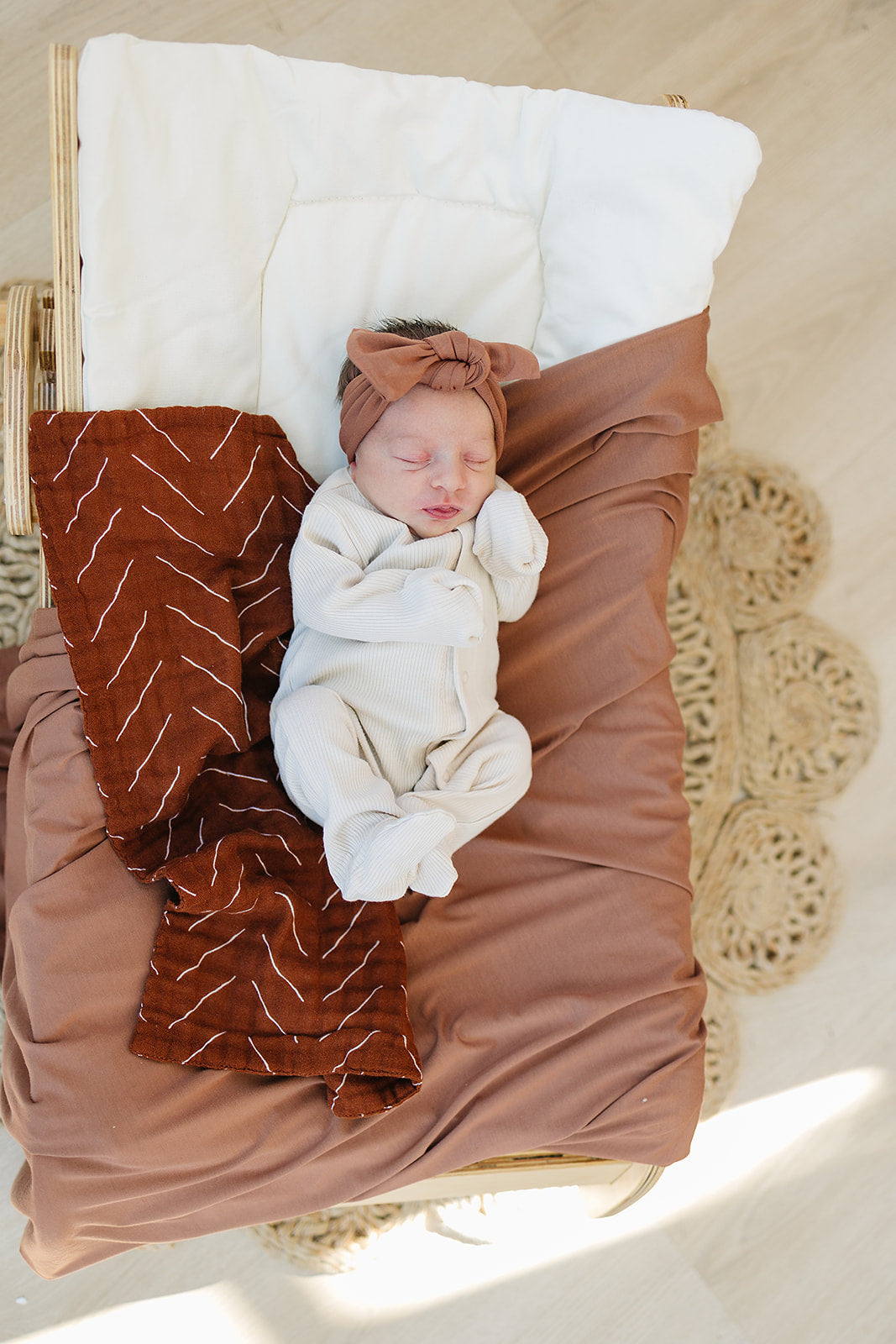 Baby peacefully sleeping in a cozy organic cotton bodysuit and headband, wrapped in a soft brown blanket.