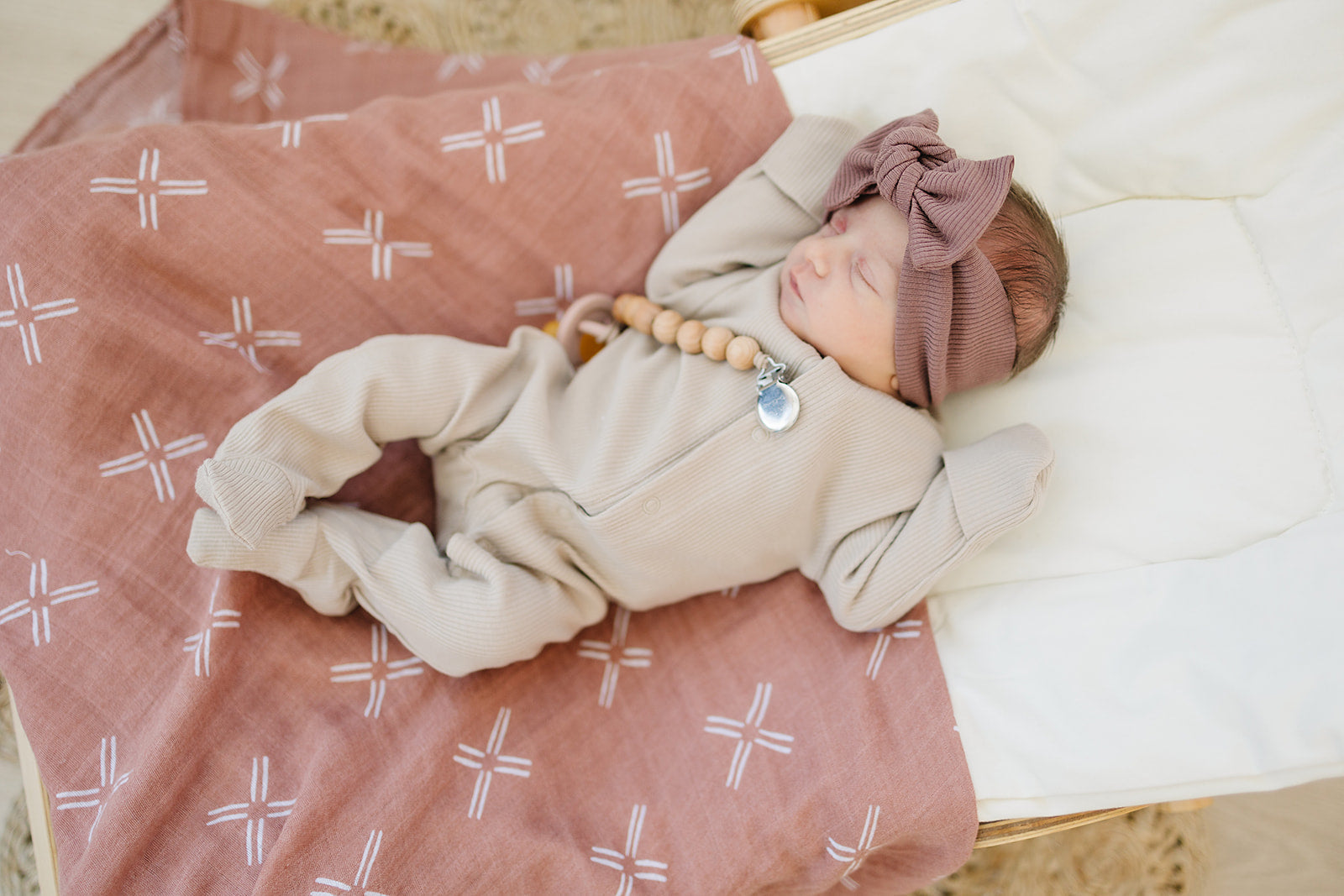 Organic baby bodysuit in oatmeal color, featuring a cozy fit, snap closures, and a cute headband on a gentle blanket.