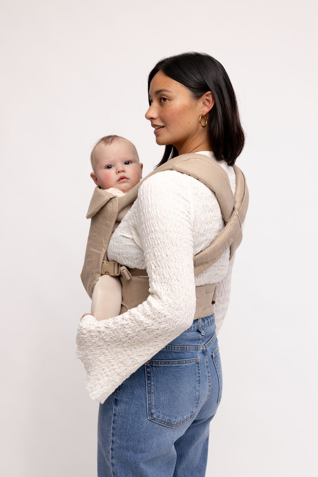 Desert Lark Aerial Carrier in cool taupe grey, worn by a woman holding a baby, showcasing comfort and style.