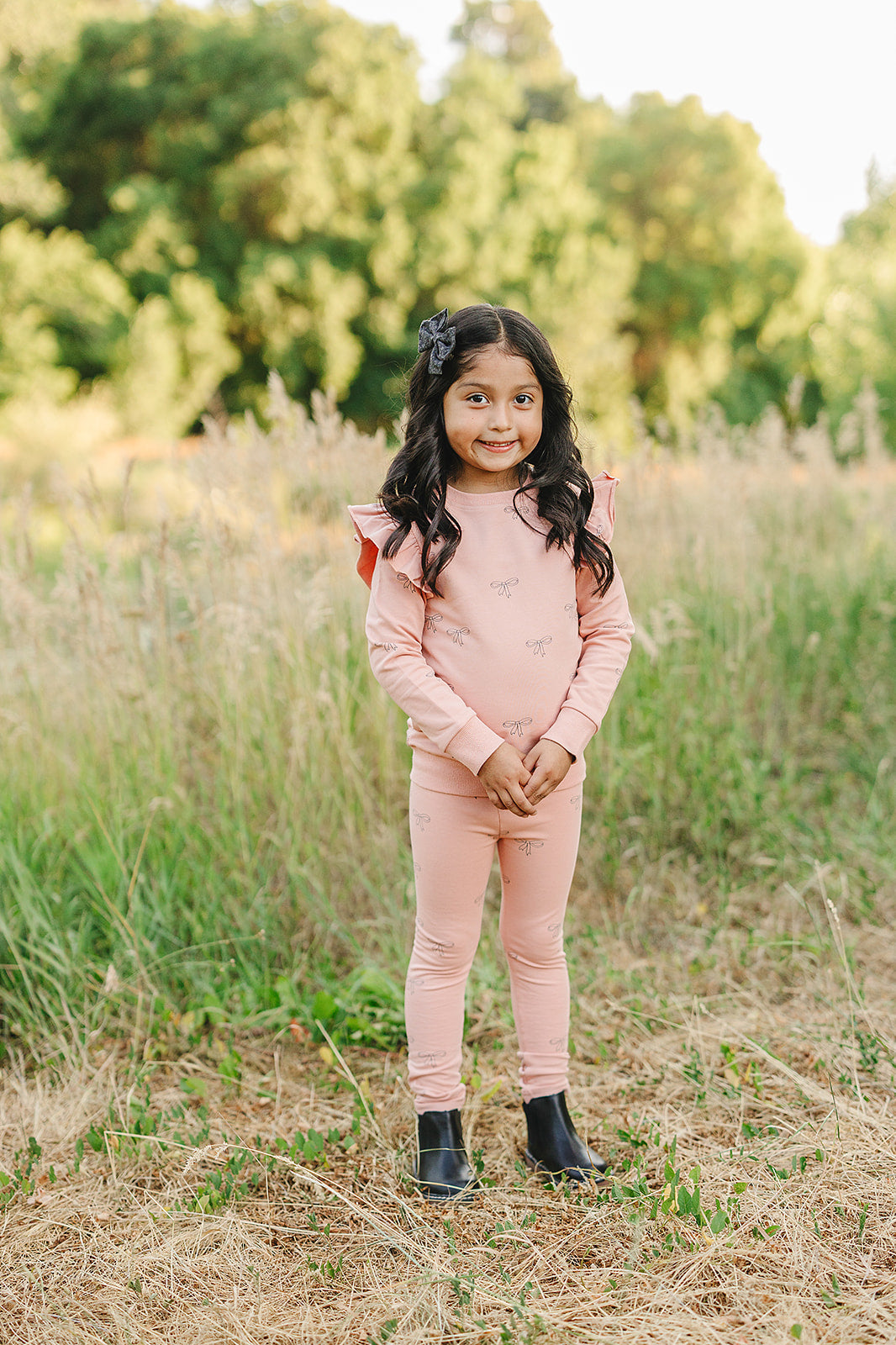 Child wearing a pink ribbon ruffle set in a grassy field, showcasing a charming French terry design.