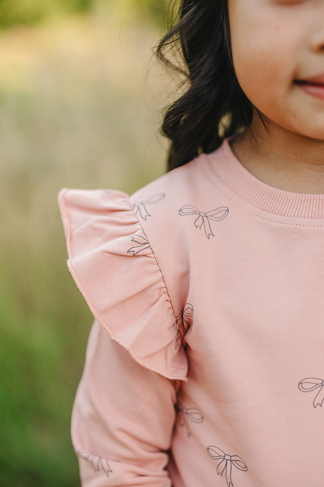 Close-up of a pink sweatshirt with ruffle sleeve detailing and ribbon print, part of the Pink Ribbon Ruffle Set.