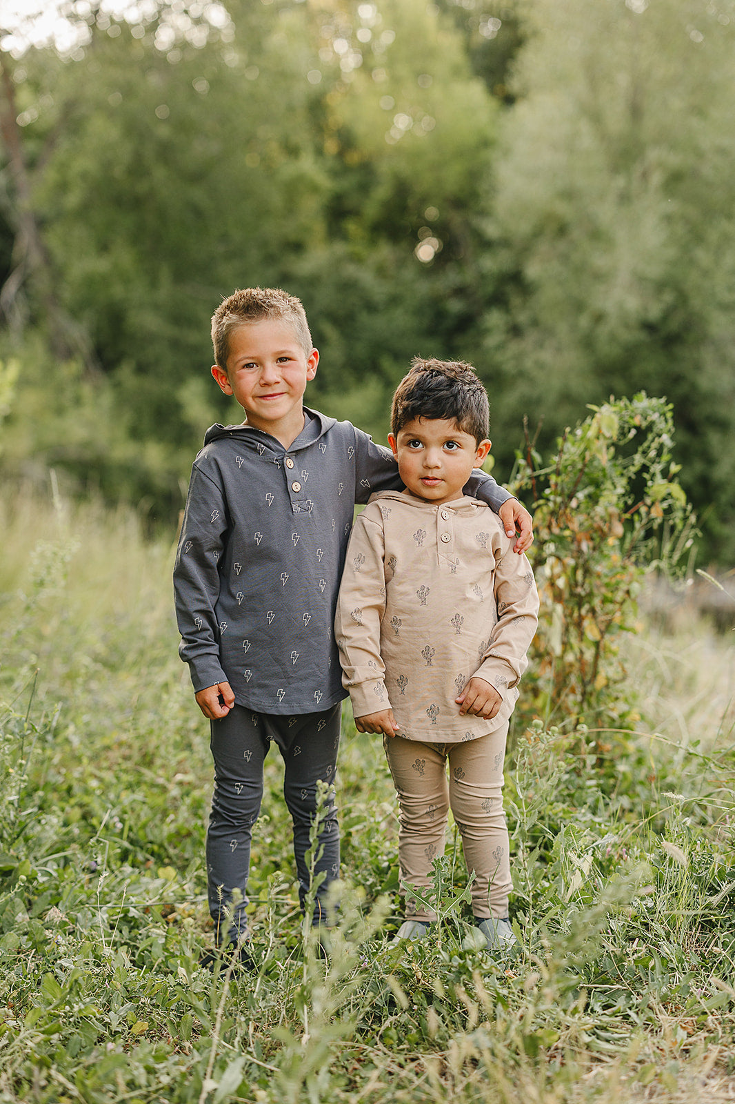 Two boys in stylish hooded outfits standing together in a grassy area, showcasing their playful school-ready looks.