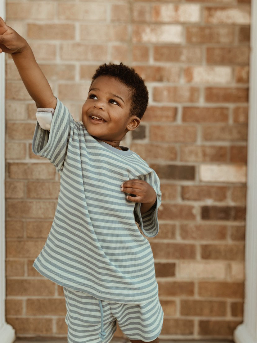 Happy toddler wearing a cotton candy two-piece short set, striking a playful pose in pastel striped outfit.