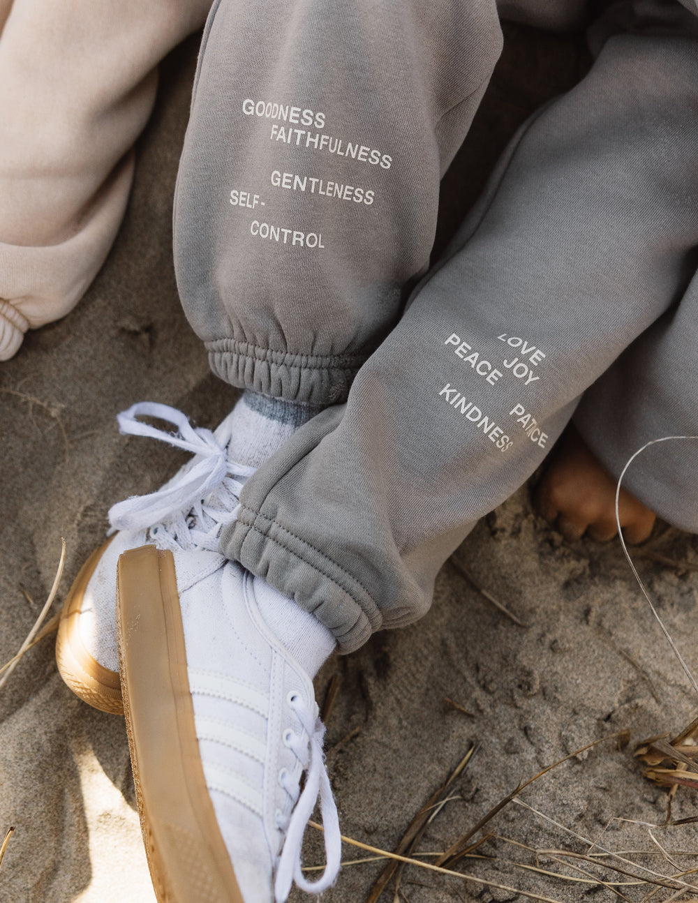 Children wearing Fruit of the Spirit kids sweatpants with inspirational text on the legs, relaxed on the sand.