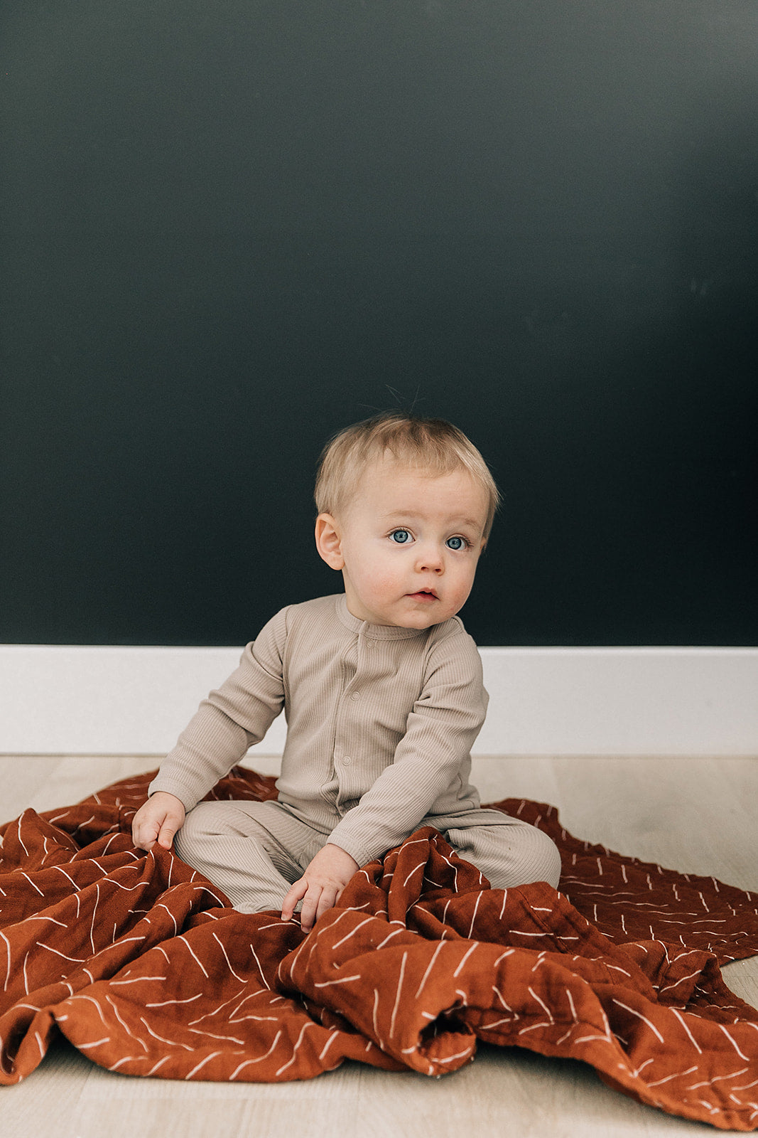 Baby in an oatmeal organic cotton ribbed bodysuit sitting on a cozy blanket, showcasing comfort and style.