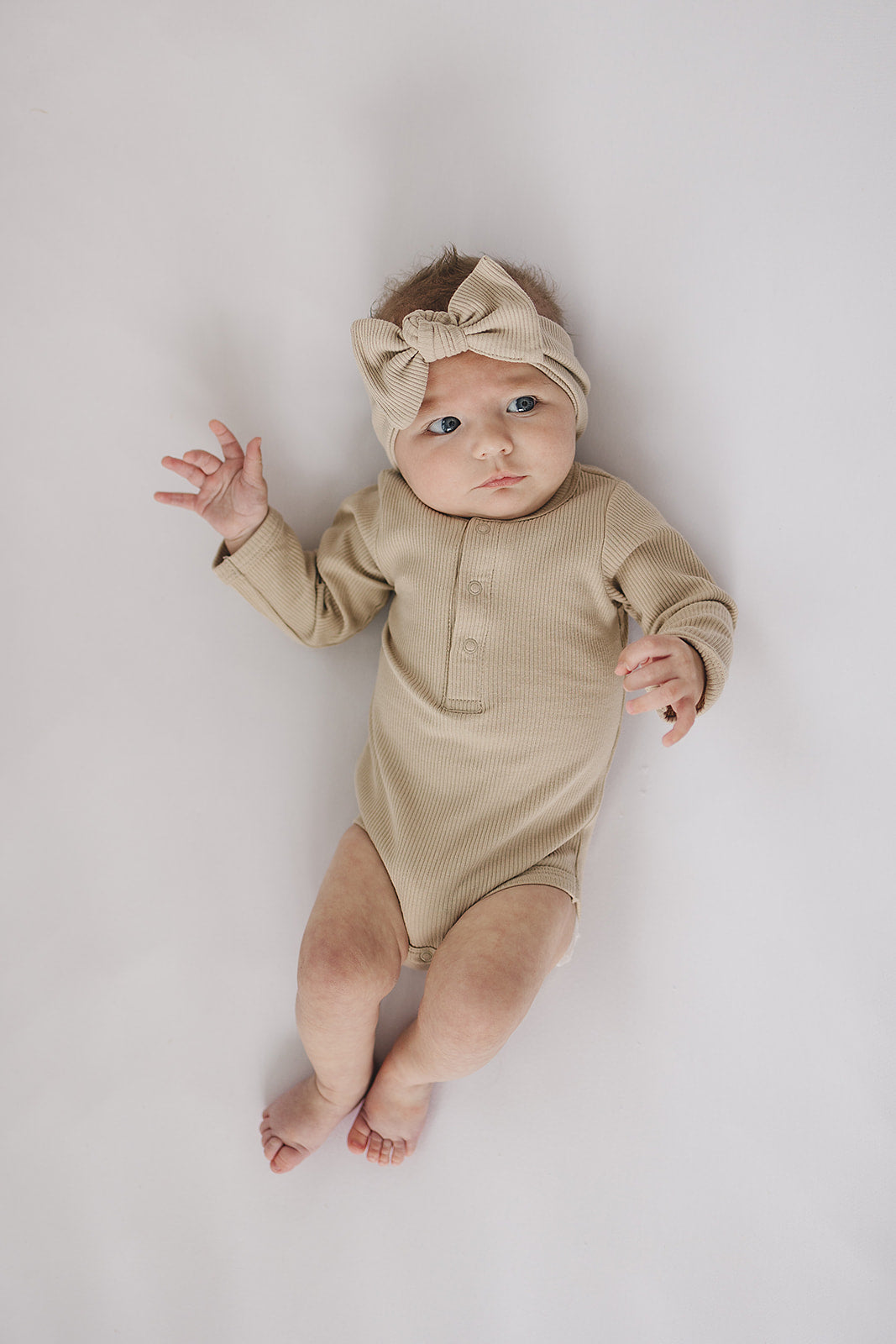 Baby in oatmeal organic ribbed bodysuit with bow headband, showcasing the ultimate organic baby bodysuit.