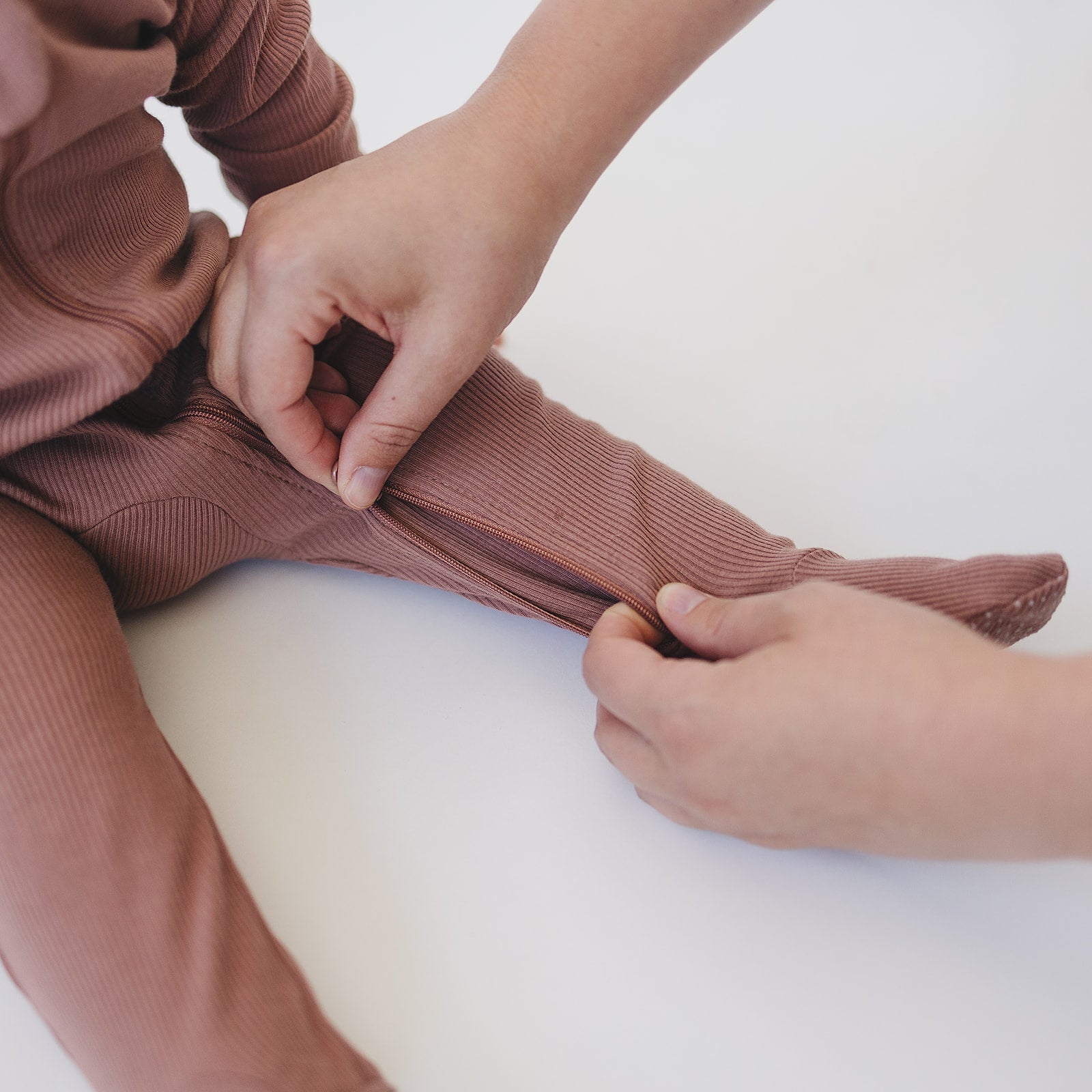 Parent zipping up the leg of a dusty rose organic baby zipper sleeper for easy dressing.