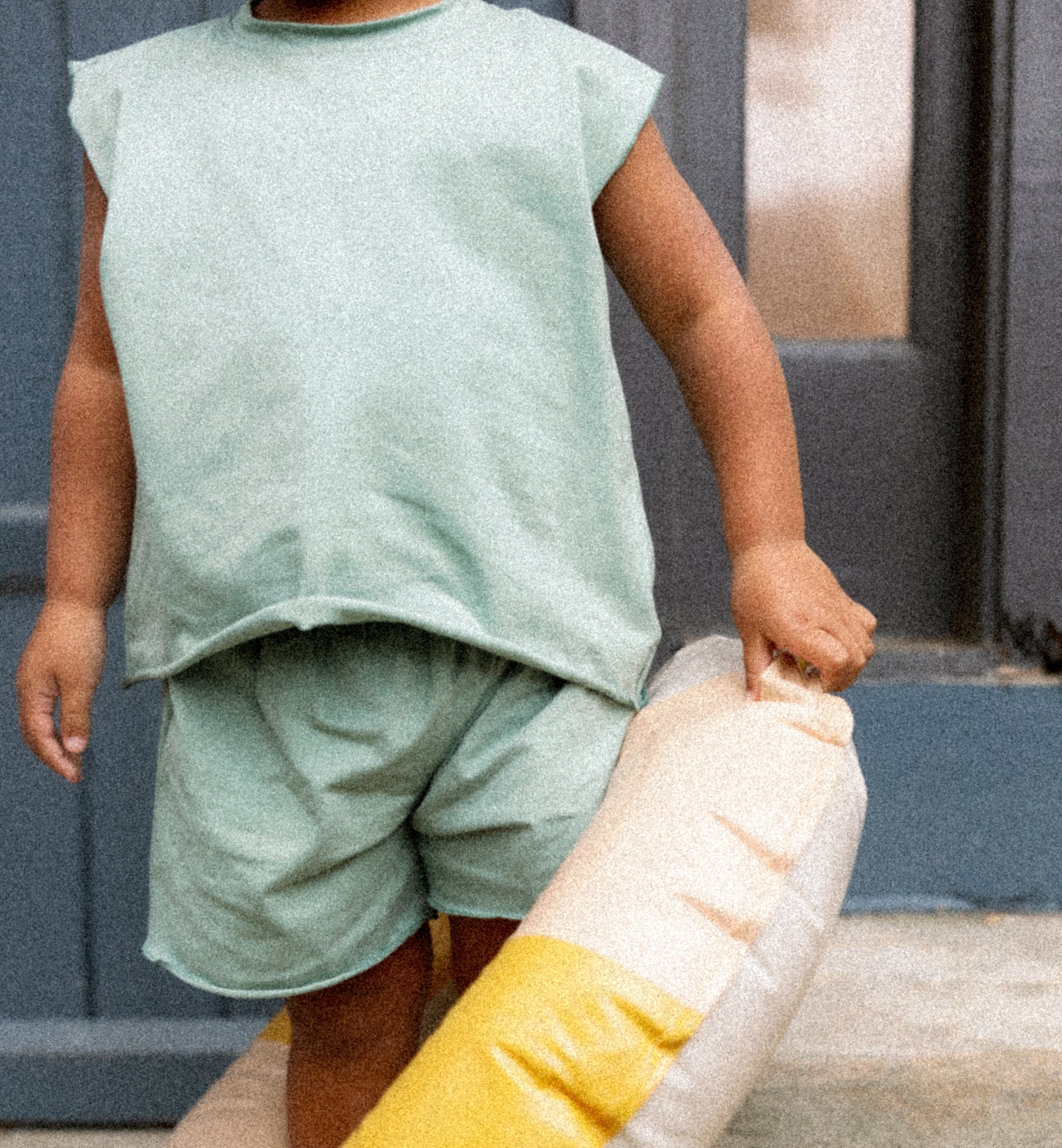 Smiling child wearing the Remy teal two-piece baby outfit, holding a pillow, showcasing cozy toddler lounge style.