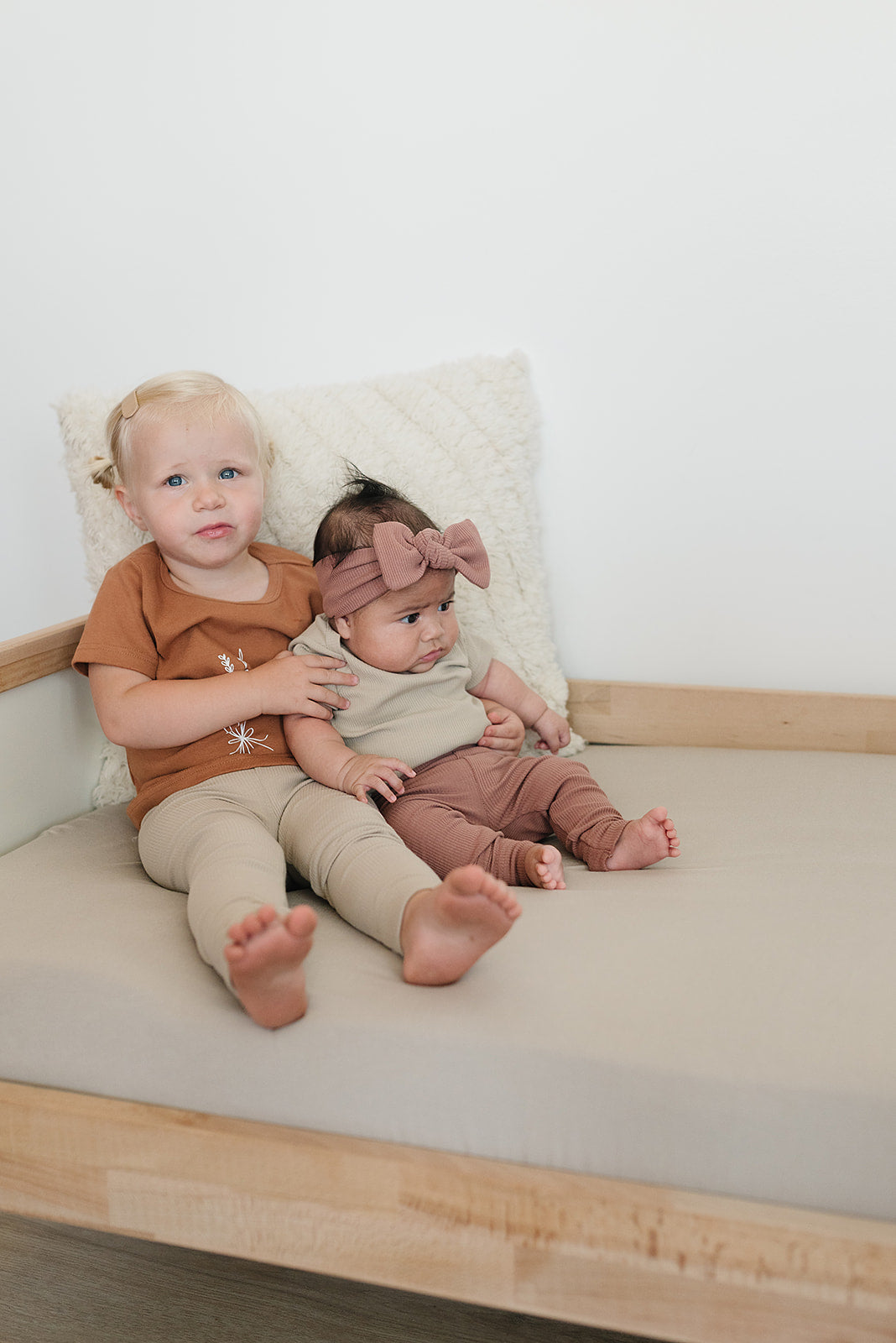 Two children sitting on a couch wearing matching organic baby leggings in soft colors, showcasing comfort and style.