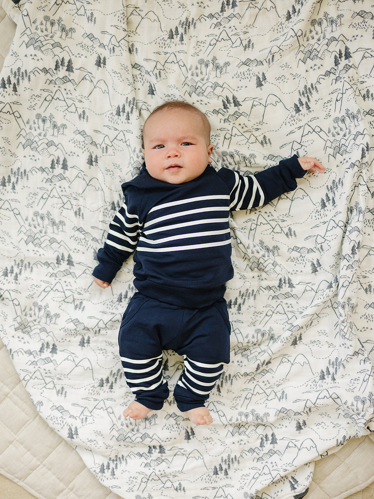 Baby wearing a navy stripes hooded French terry set on a patterned blanket, perfect boys school outfit.