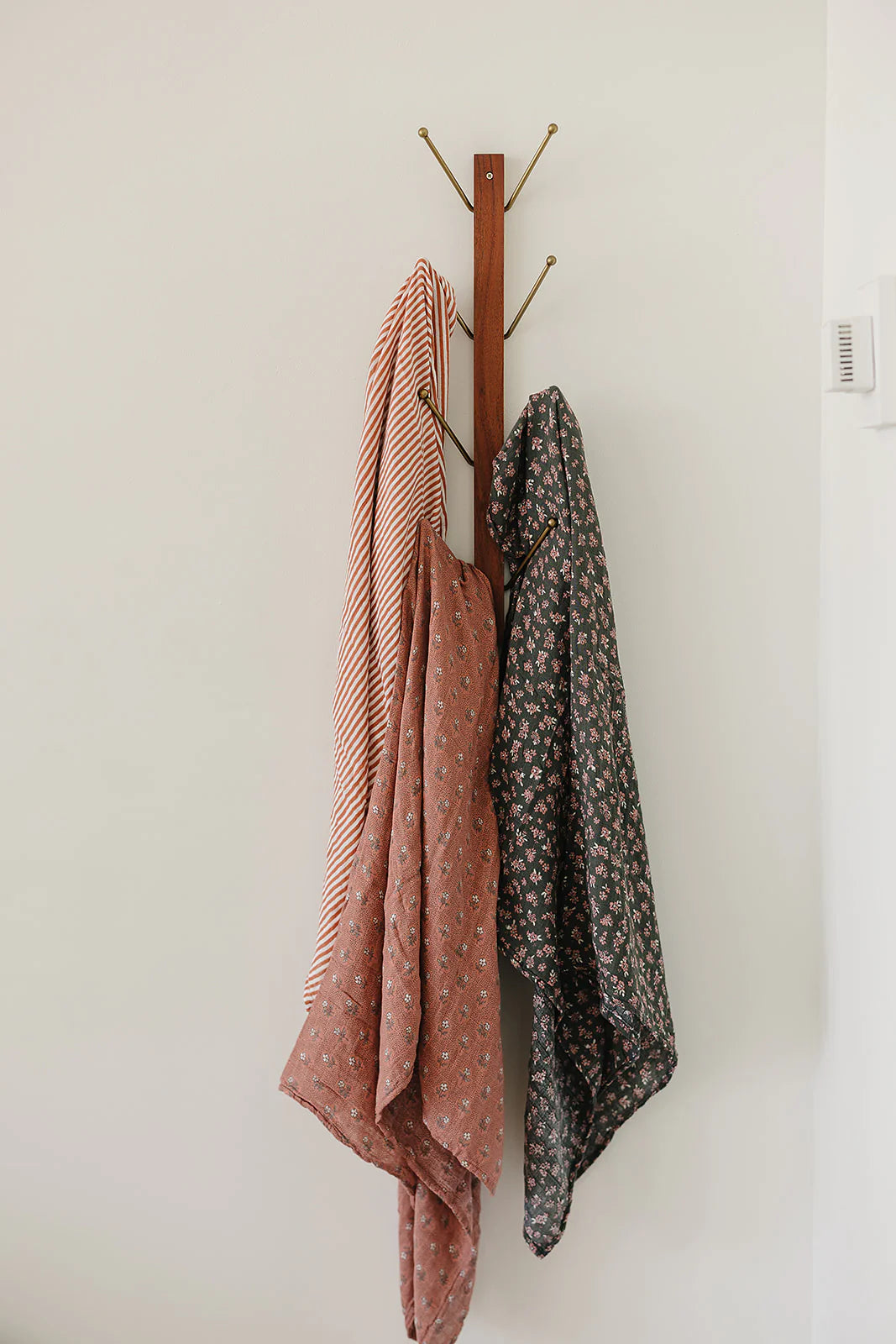Three stylish muslin blankets hanging on a hook, showcasing modern patterns and colors for versatile use in any setting.