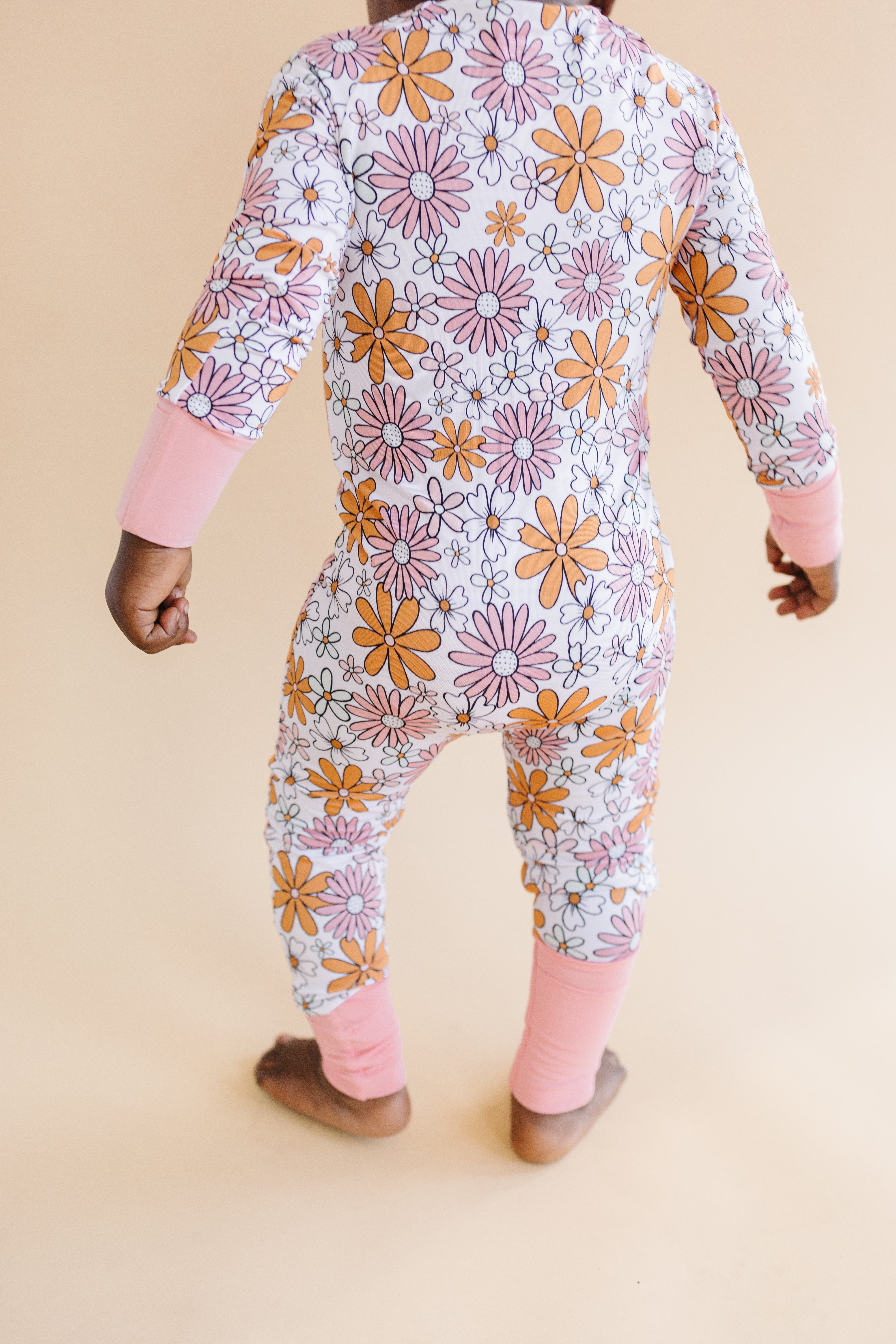Bamboo zip baby romper with floral print, showcasing bright daisies and soft pink cuffs, ideal for comfort during playtime.