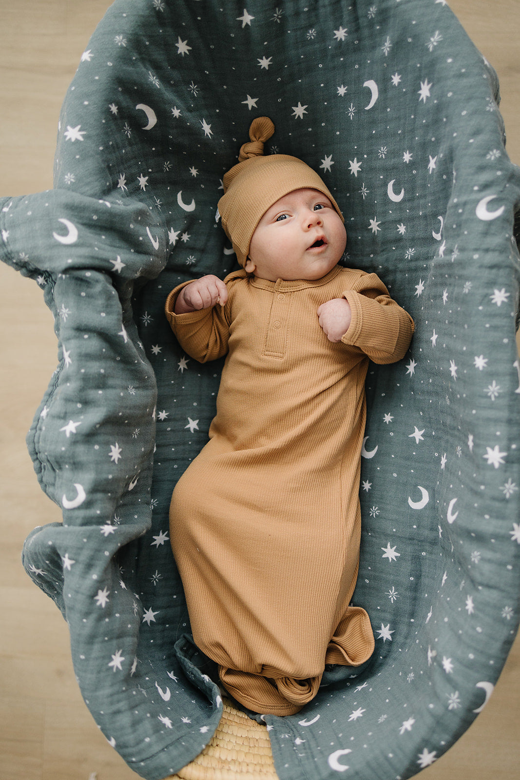 Baby in a cafe brown outfit lying in a grey crib with star and moon pattern