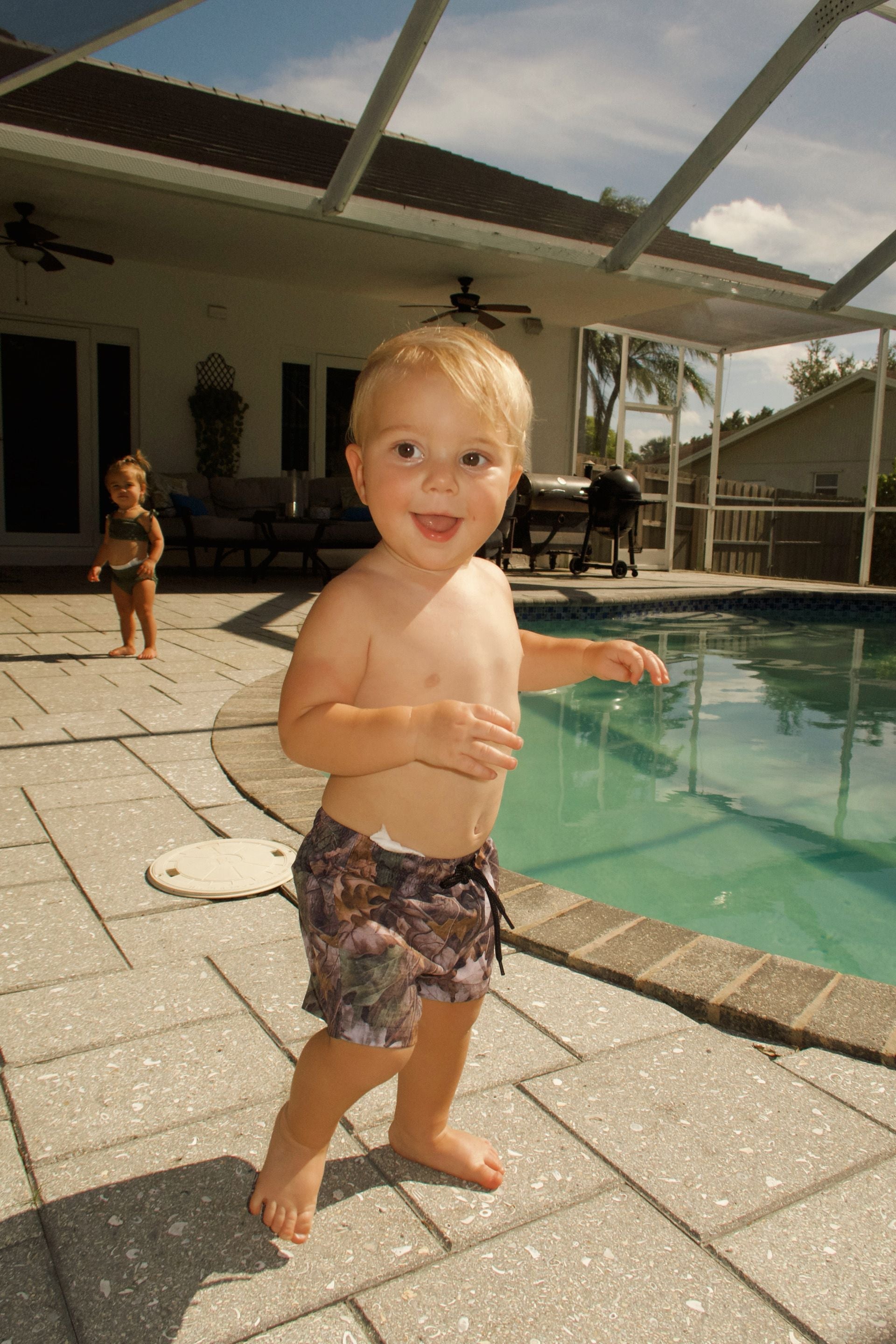 Toddler wearing camo swim shorts by the pool, enjoying summer activities, ready for water play.