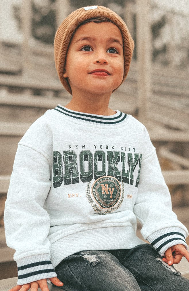 Toddler wearing vintage inspired Brooklyn crew sweatshirt with retro graphic and beanie, styled for comfort.
