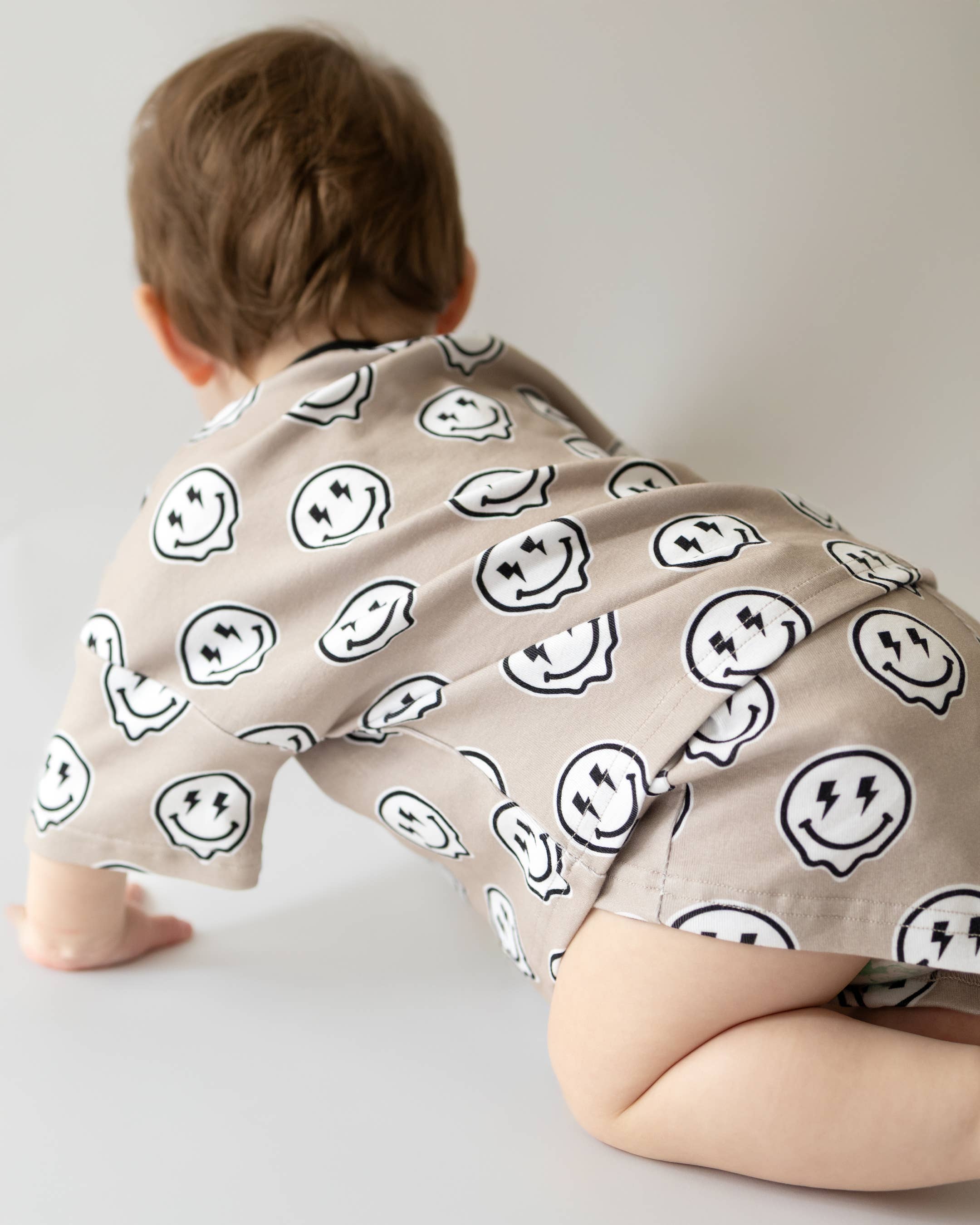 Toddler wearing Electric Drippy shorts set with smiley face print, crawling on the floor.