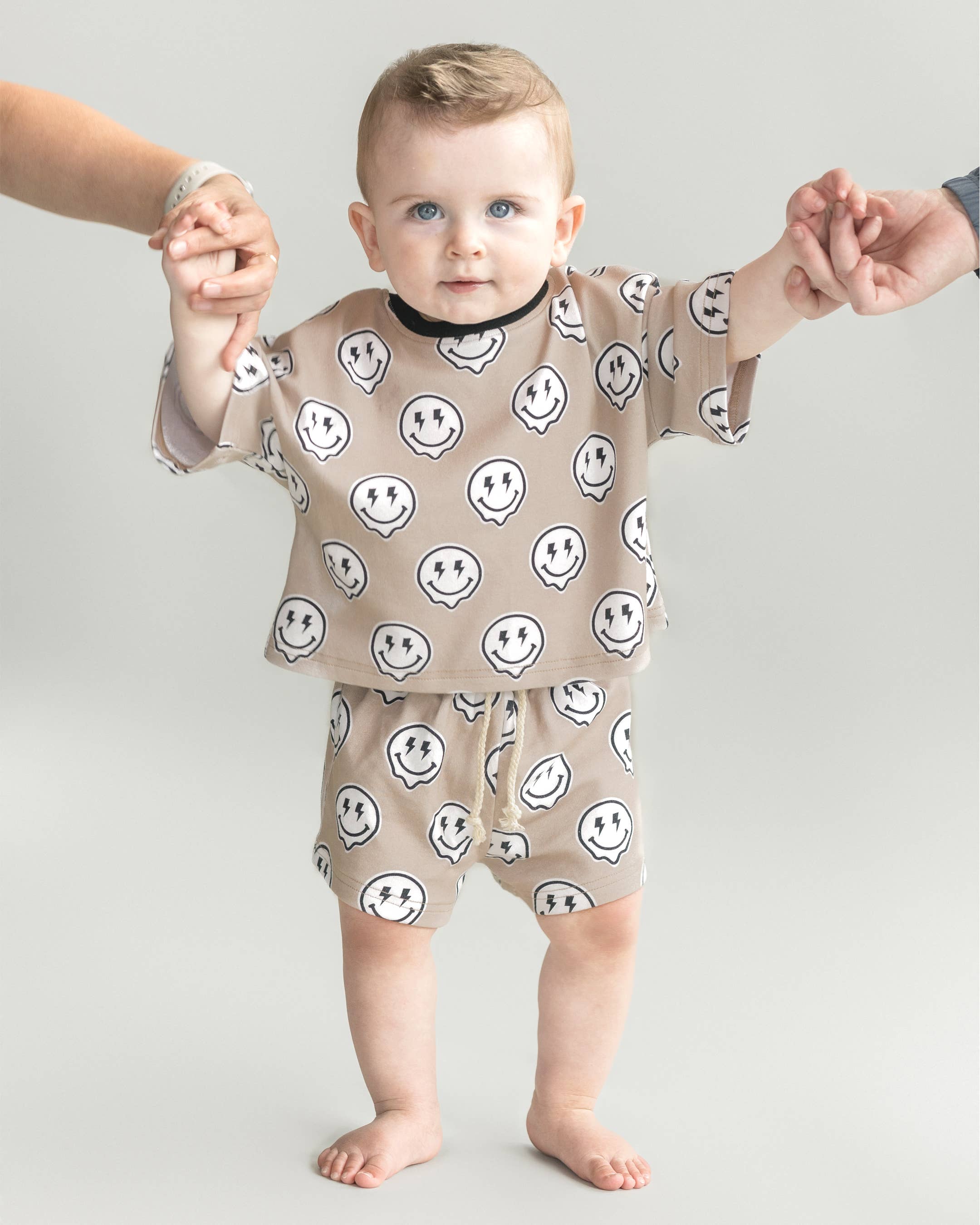 Toddler wearing Electric Drippy shorts set with smiley face print, held by adults, showcasing streetwear style.