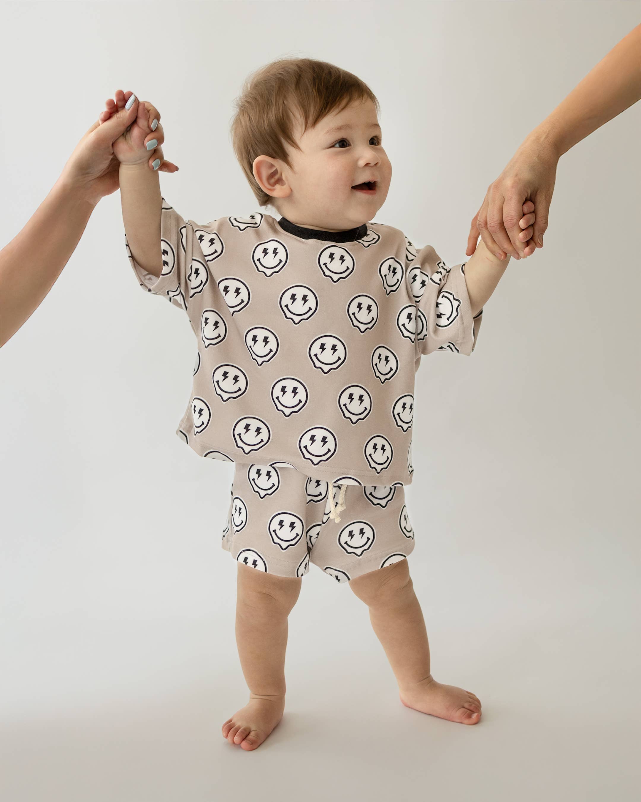 Toddler wearing Electric Drippy shorts set with smiley face print, held by adults, showcasing streetwear style.
