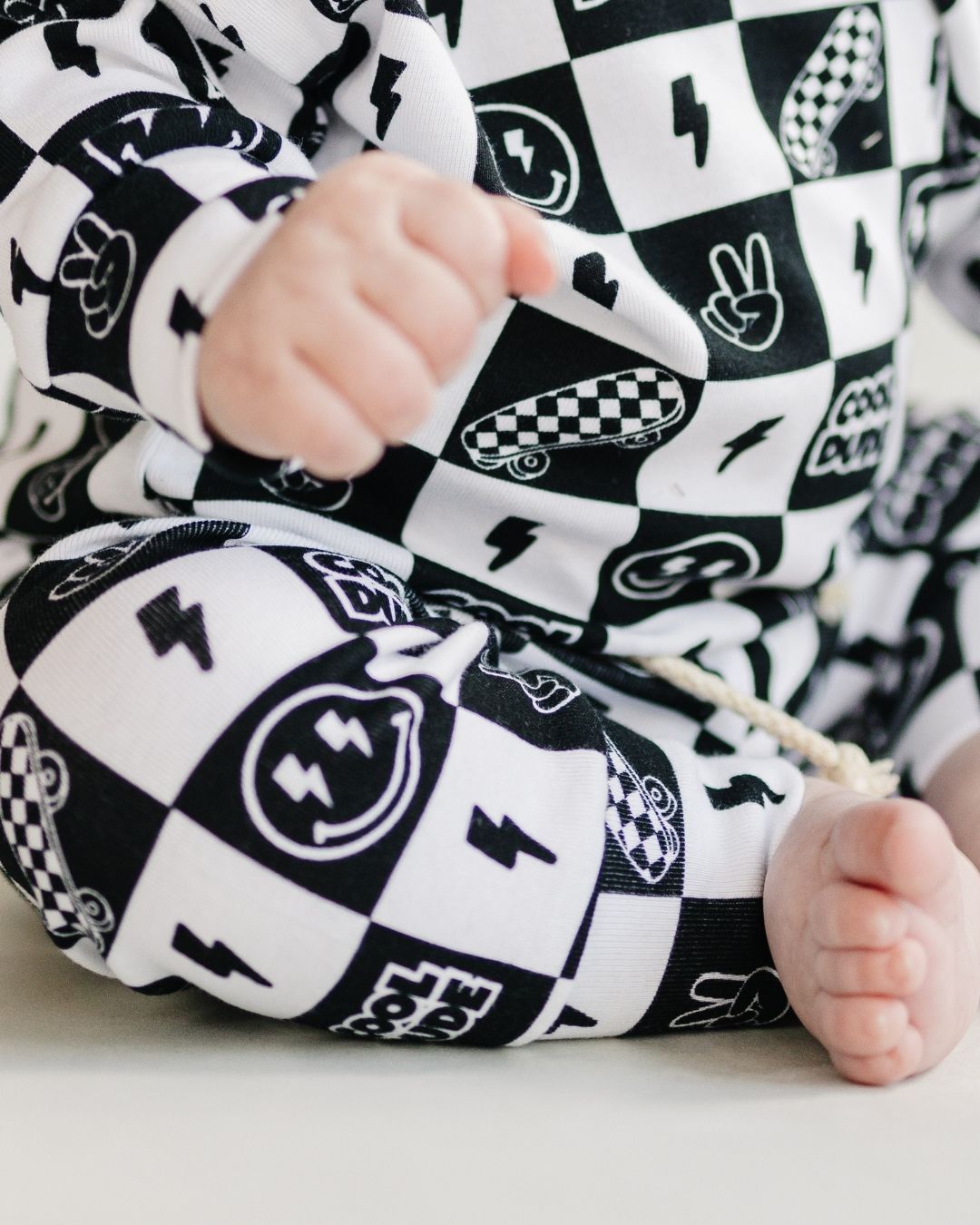 Close-up of a baby's arm and leg in a black and white checkered jogger set with playful graphics.