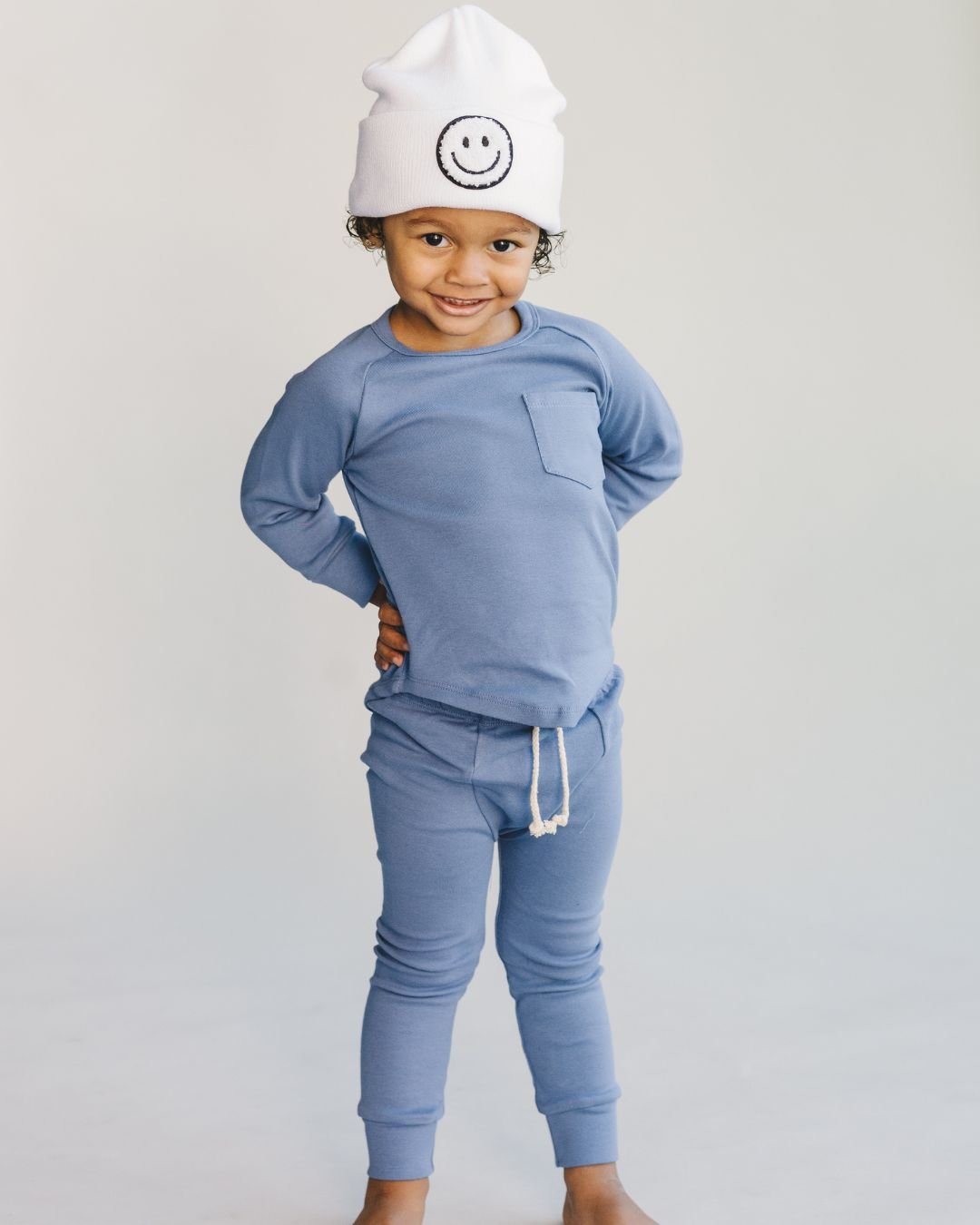 Child wearing lounge set ocean blue with smiley face beanie, featuring a cozy top and pants design.