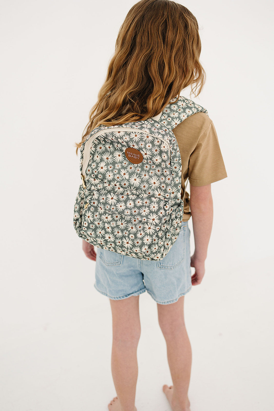 Child wearing a green daisy mini backpack, ideal kids mini backpack for preschool and playdates.