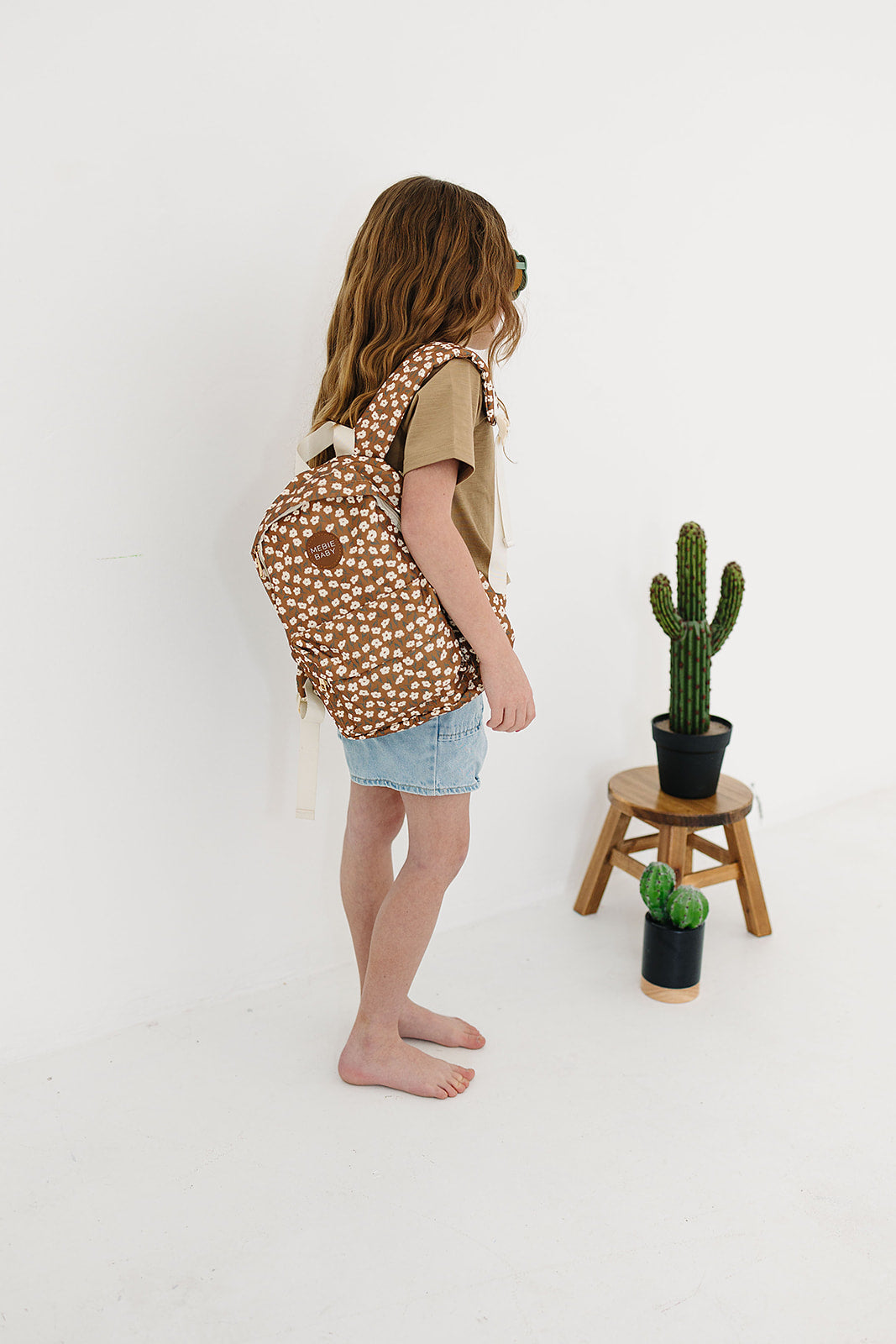 Child wearing a mustard floral mini backpack, showcasing its playful design, perfect for kiddos on the go.