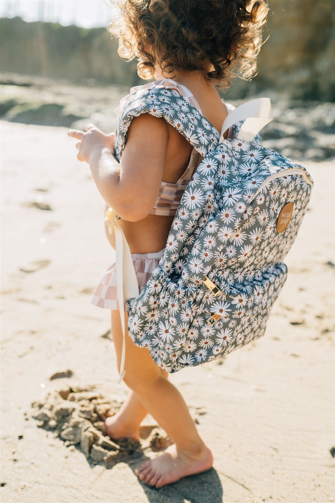Kids mini backpack with daisy print worn by a child on the beach, ideal for little explorers.