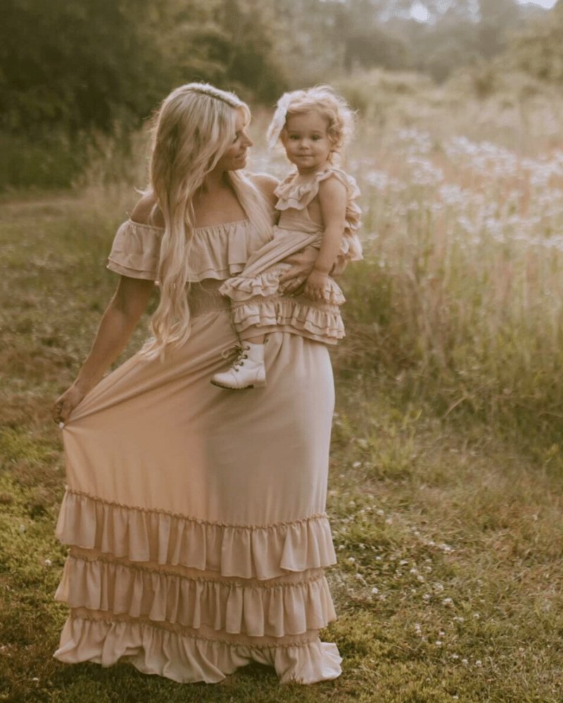 Mom and daughter in matching champagne dresses with ruffles, enjoying a moment outdoors in a sunny field.