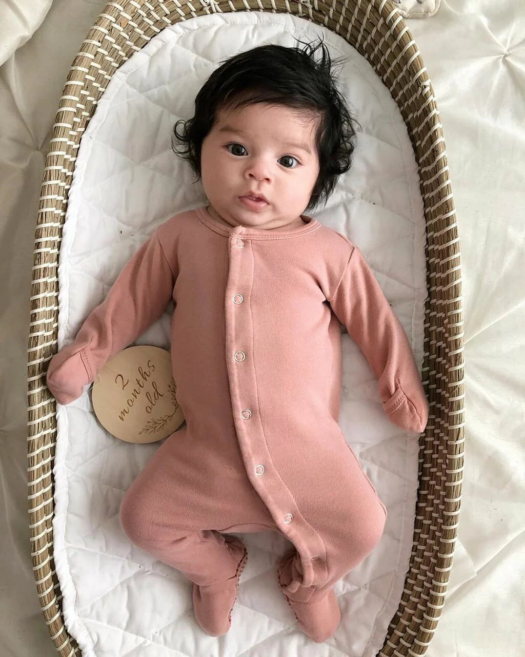 Baby in mauve organic snap footie lying on a soft surface, showcasing its cozy design and front snaps for easy changing.