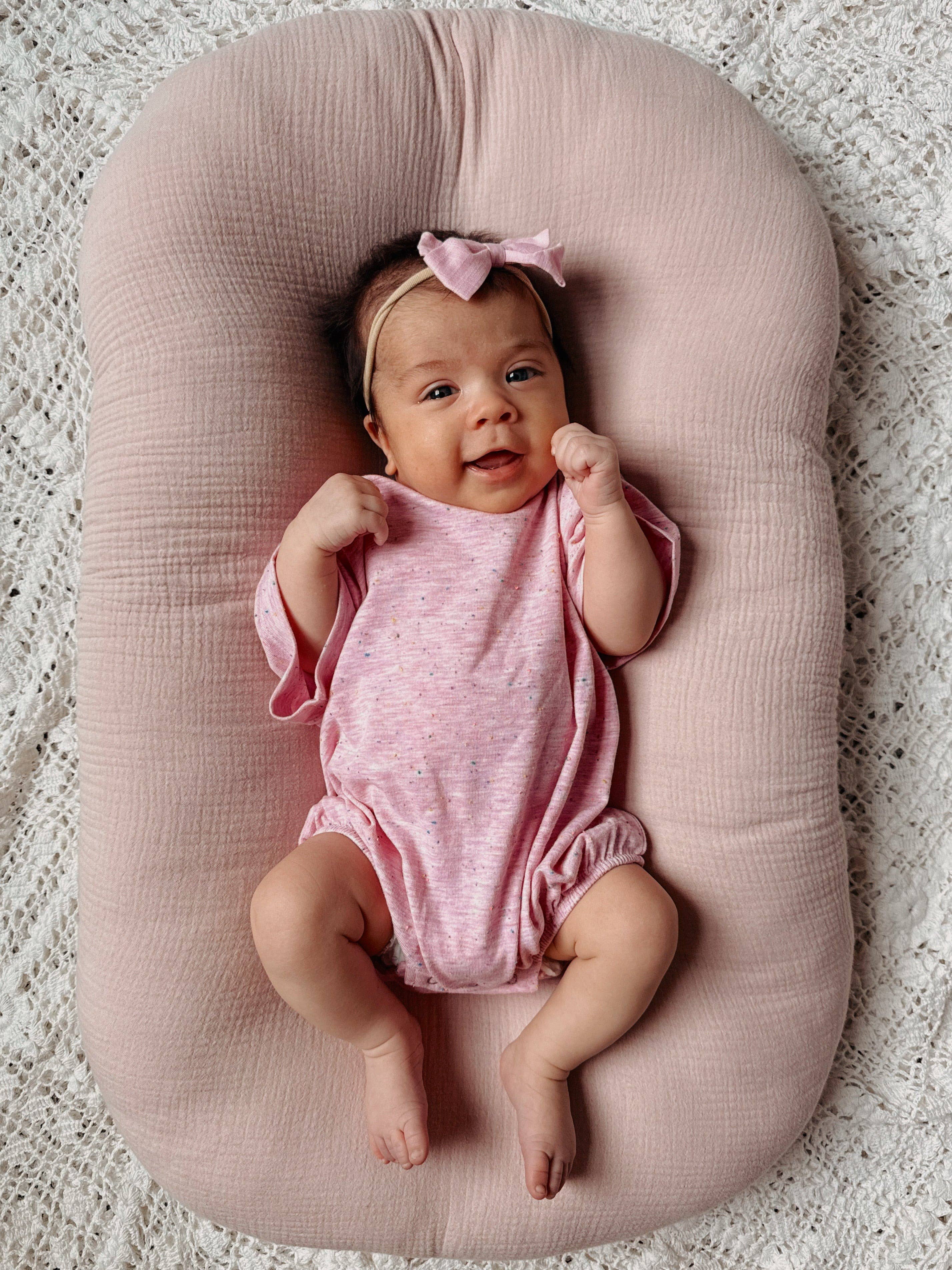 Baby girl in pink speckle t-shirt bubble lying on a soft surface, smiling and wearing a cute bow headband.