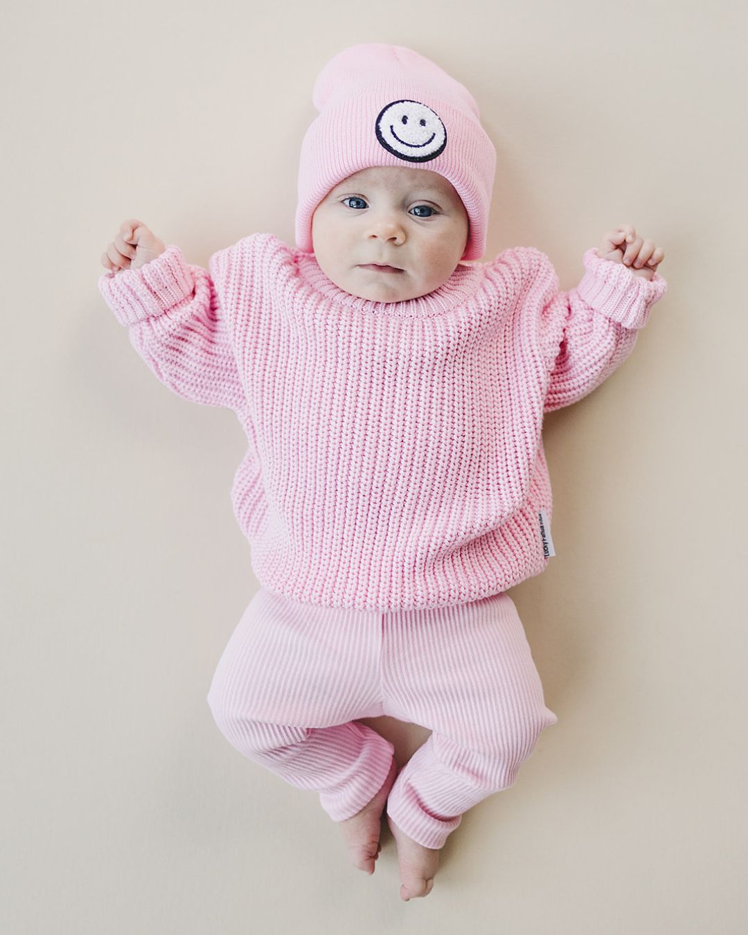 Infant wearing a pink Smiley Beanie and matching sweater outfit, perfect for cozy warmth and adorable style.