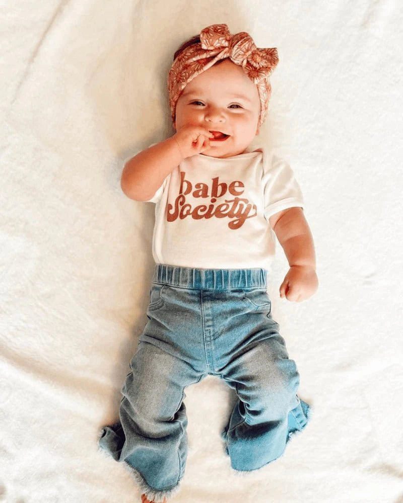 Toddler girl wearing light wash bell bottom jeans and a 'Babe Society' shirt with a stylish headband.