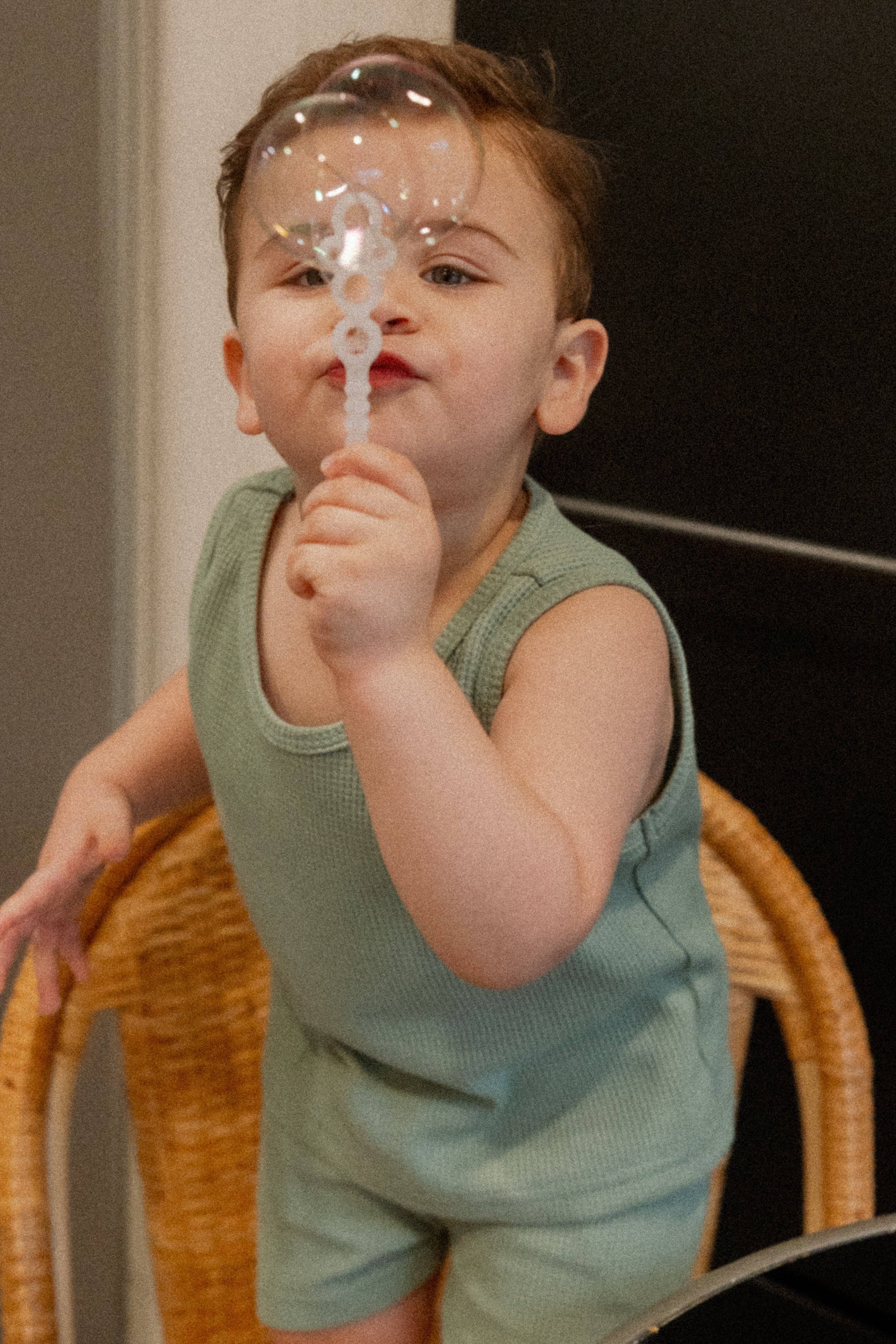 Toddler in teal summer tank and shorts, blowing a bubble, capturing playful and fun summer vibes.