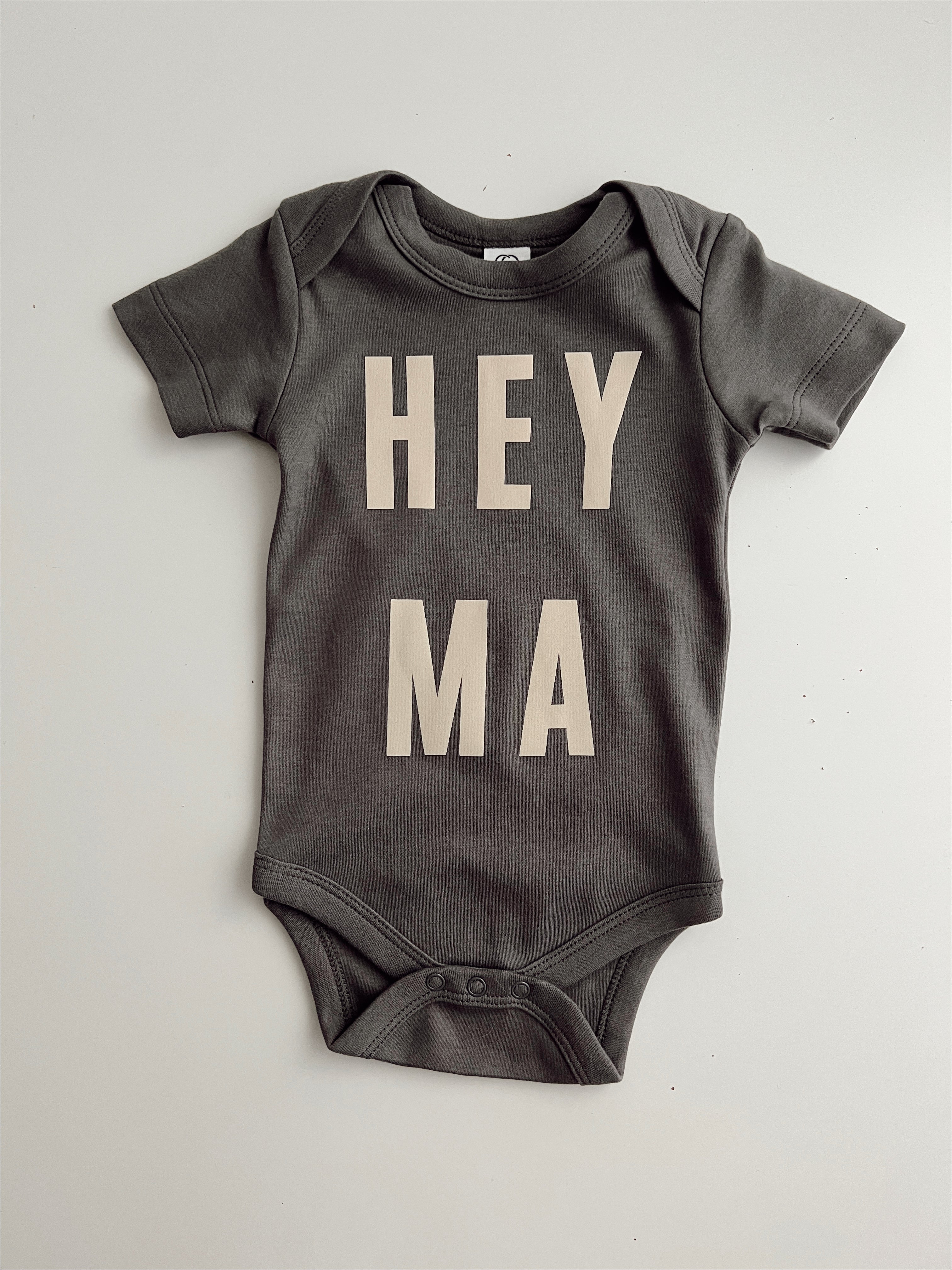 Organic baby onesie in dark gray with 'HEY MA' design, perfect for trendy, cool moms and their little stars.