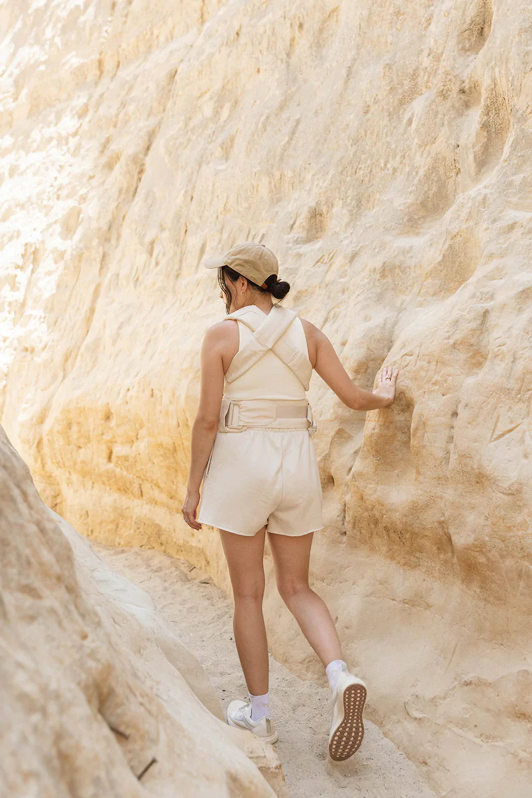 Woman wearing a beige Sparrow Aerial Carrier in a sandy canyon, showcasing stylish straps and a classic design.