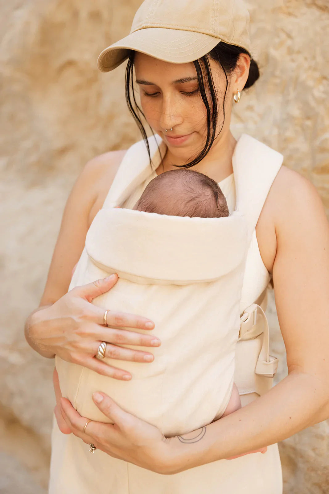 A mother wearing the Sparrow Aerial Carrier in vanilla beige, securely holding her baby close.