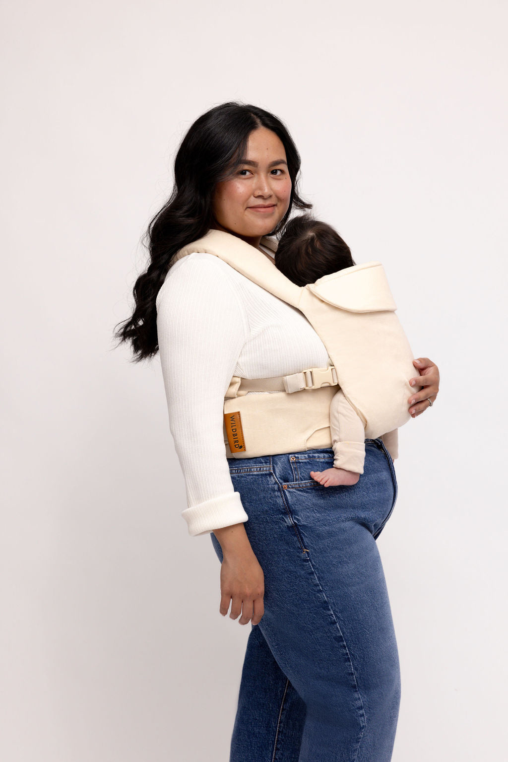 Woman wearing the Sparrow Aerial Carrier in vanilla beige, holding a baby, showcasing color-matched straps and mesh design.