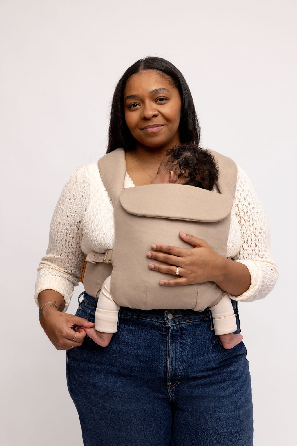 Woman wearing a taupe grey Desert Lark aerial carrier with a baby inside, showcasing comfort and style.