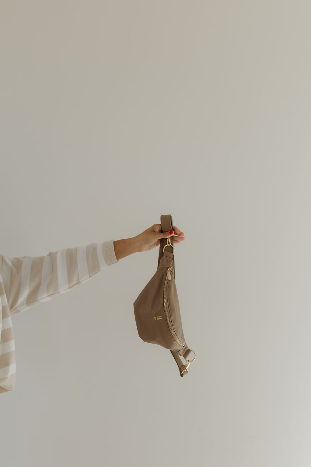 Hand holding the ff belt bag taupe, a stylish faux leather accessory with gold hardware.